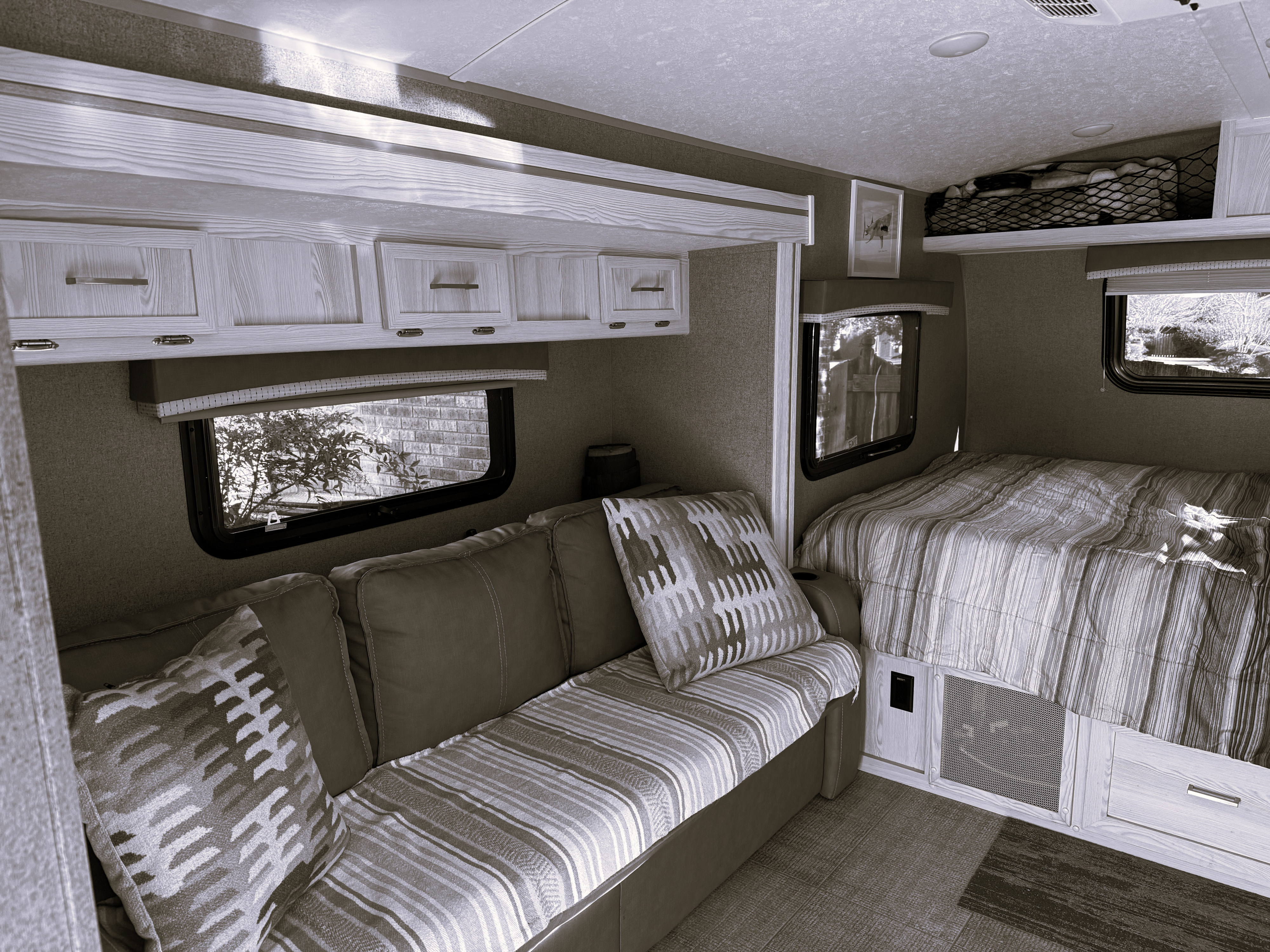 Cozy sepia-toned RV rental interior with a sofa, patterned cushions, overhead cabinets, and a comfortable bed.. Forest River Rockwood Geo Pro 2021