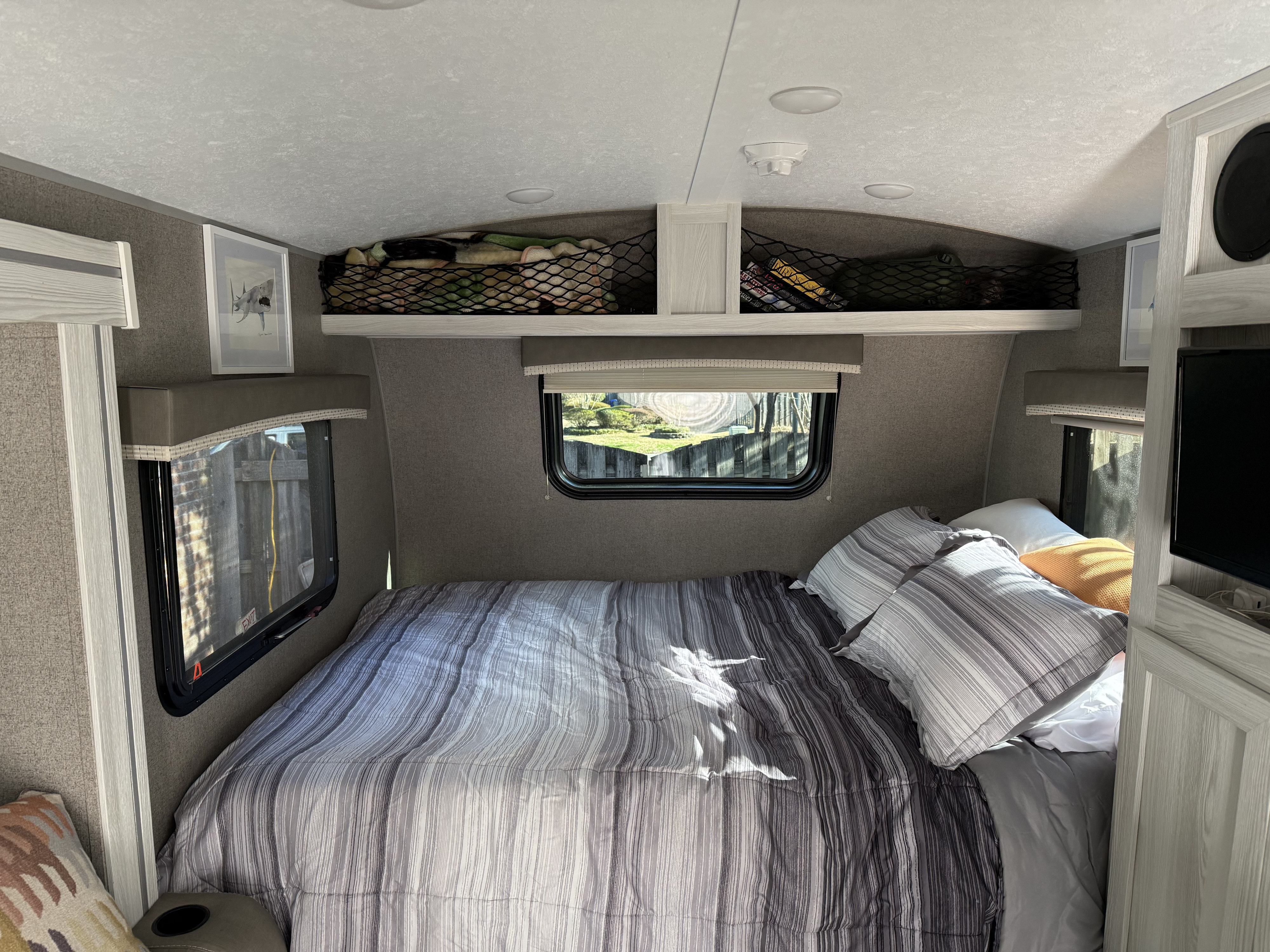 RV rental bedroom featuring a comfy bed with striped bedding, windows for natural light, and handy overhead storage nets.. Forest River Rockwood Geo Pro 2021
