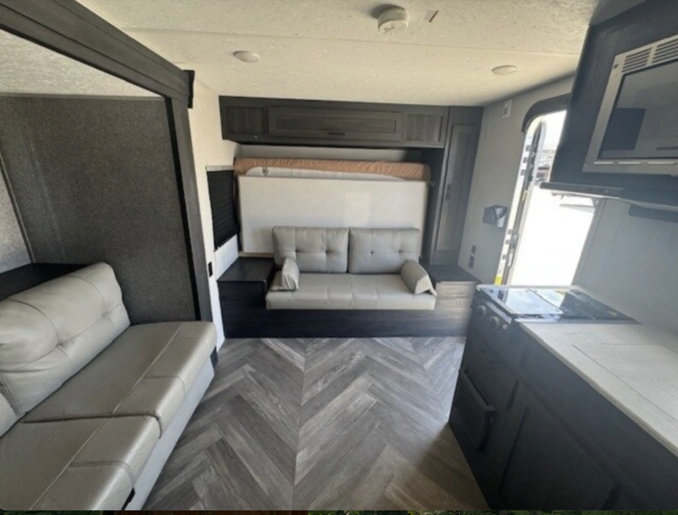 RV rental interior: living area with light grey sofas, convertible bed, and kitchen with dark cabinets & herringbone floor.. Forest River OZARK 1680BSKX 2021