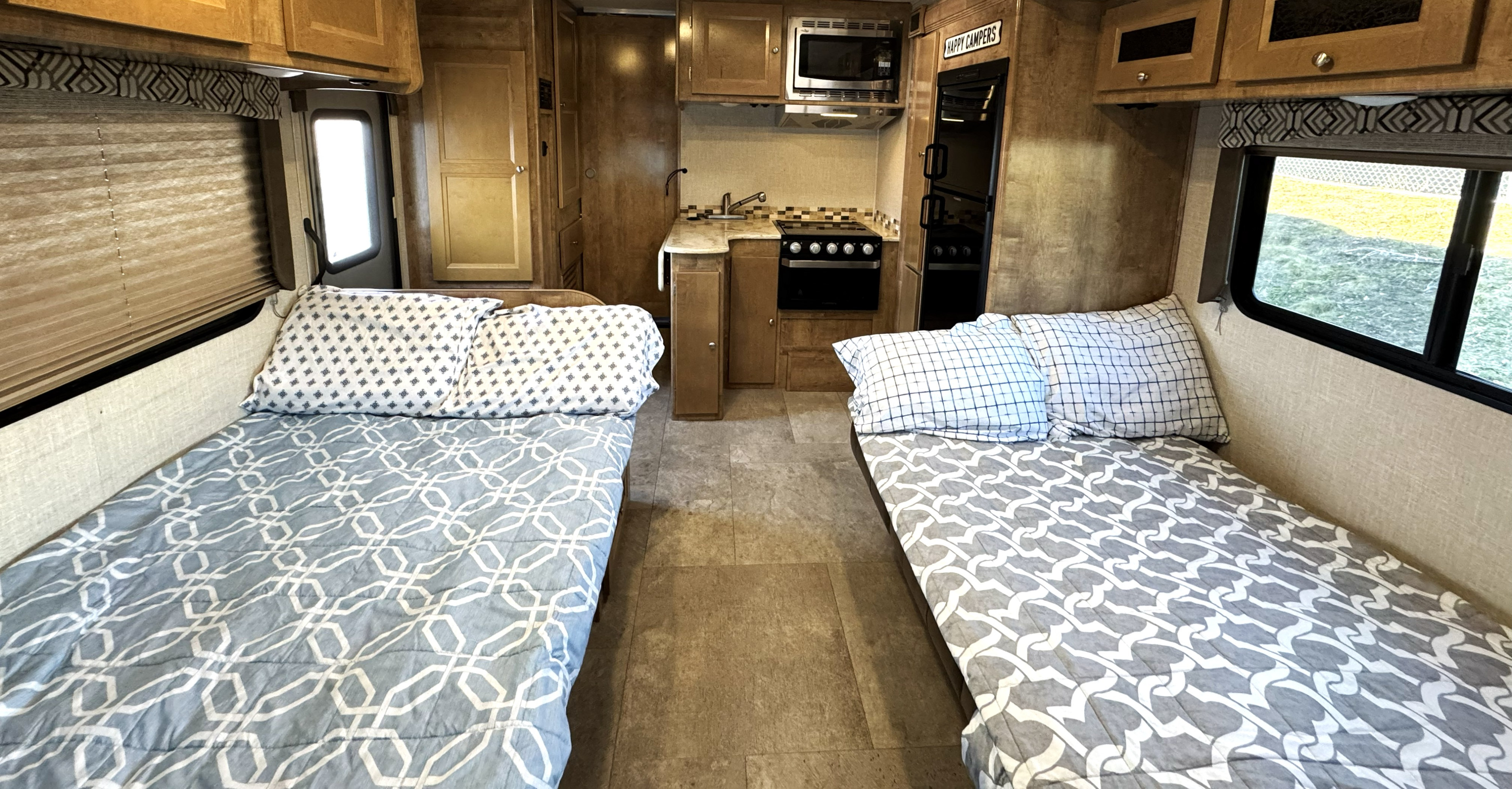 Inside an RV rental: a neat kitchen area with stove, sink, and microwave, flanked by two cozy twin beds with patterned bedding.. Coachmen Leprechaun 2020