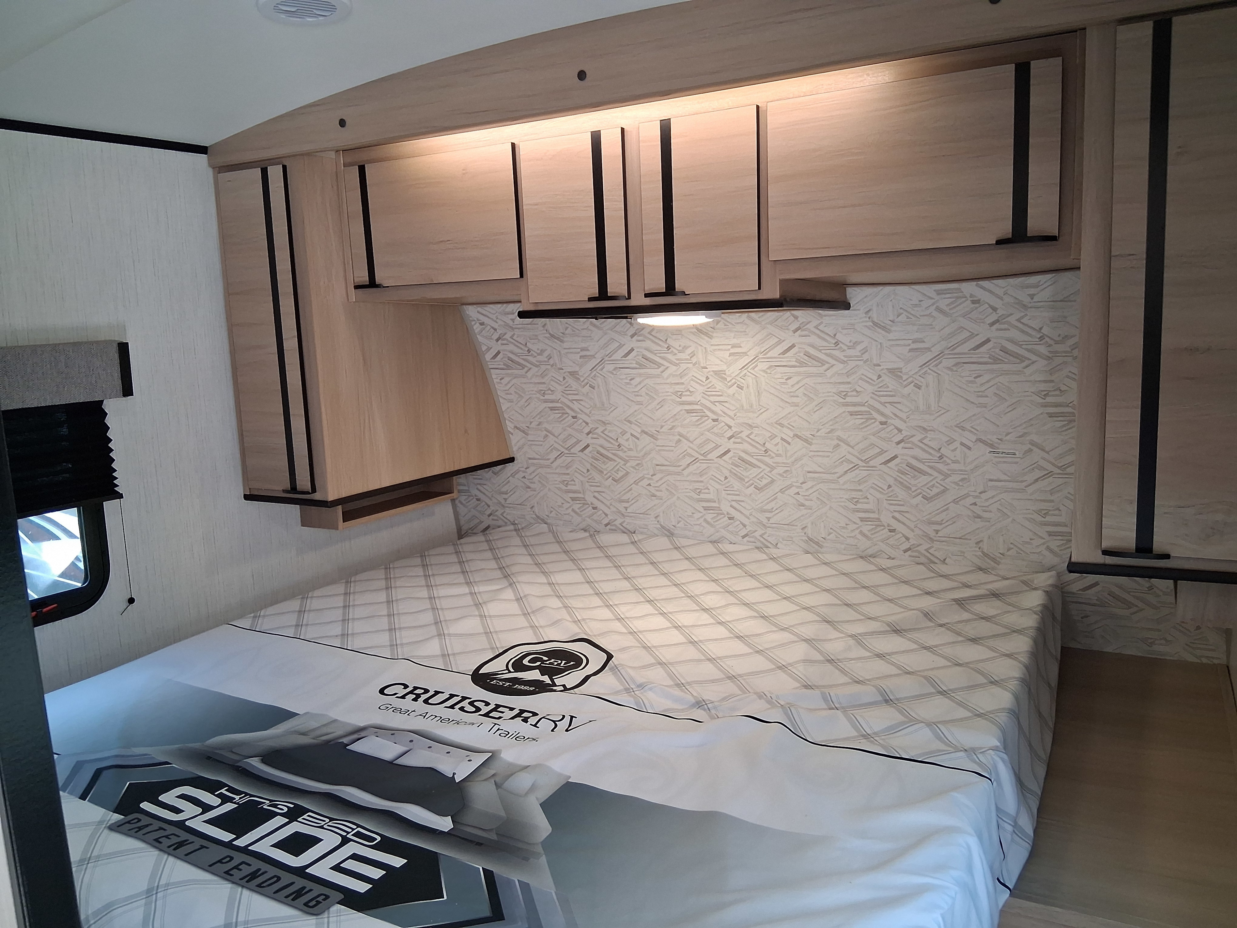 RV rental bedroom featuring a 'King Bed Slide' mattress, light wood cabinets, and patterned wallpaper, perfect for a cozy stay.. Cruiser RV Radiance 2022