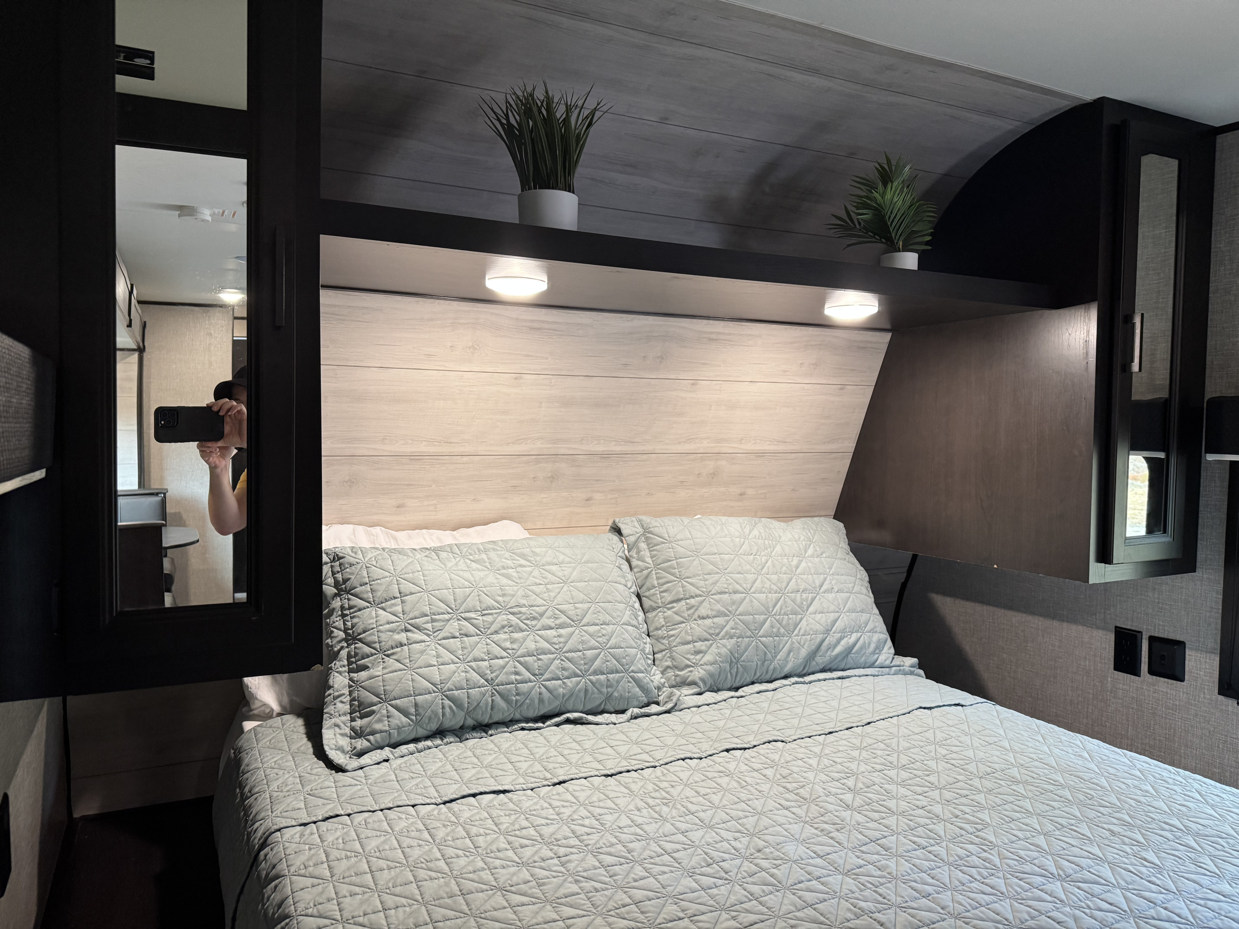 Cozy RV rental bedroom features a comfy bed with quilted bedding, a modern headboard with reading lights, and decorative plants.. Jayco Jay Flight 2022