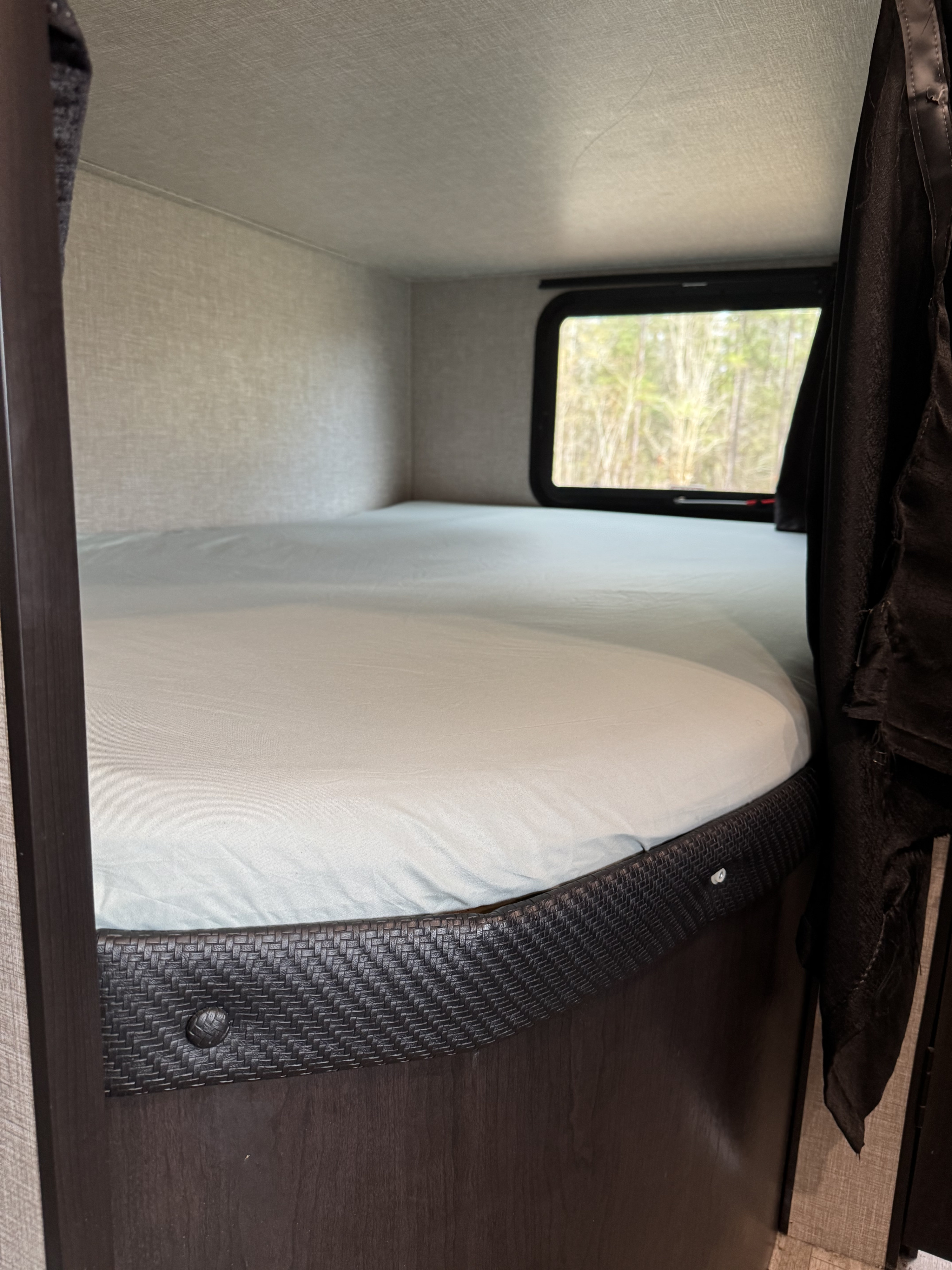 An inviting rv rental bunk bed, featuring light blue sheets and a window looking out to trees, for a comfortable stay.. Jayco Jay Flight 2022
