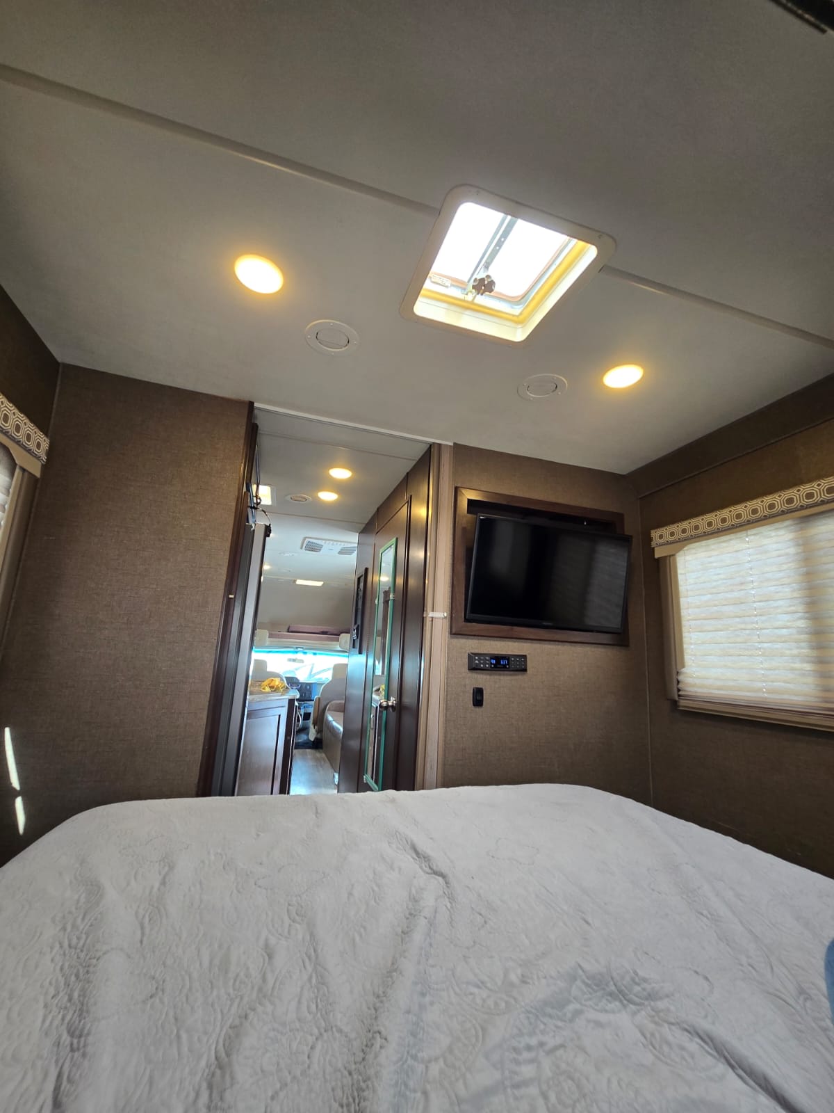 An inviting RV rental bedroom with a comfy bed, mounted TV, ceiling skylight, and a clear path to the front.. Thor Four Winds 2019