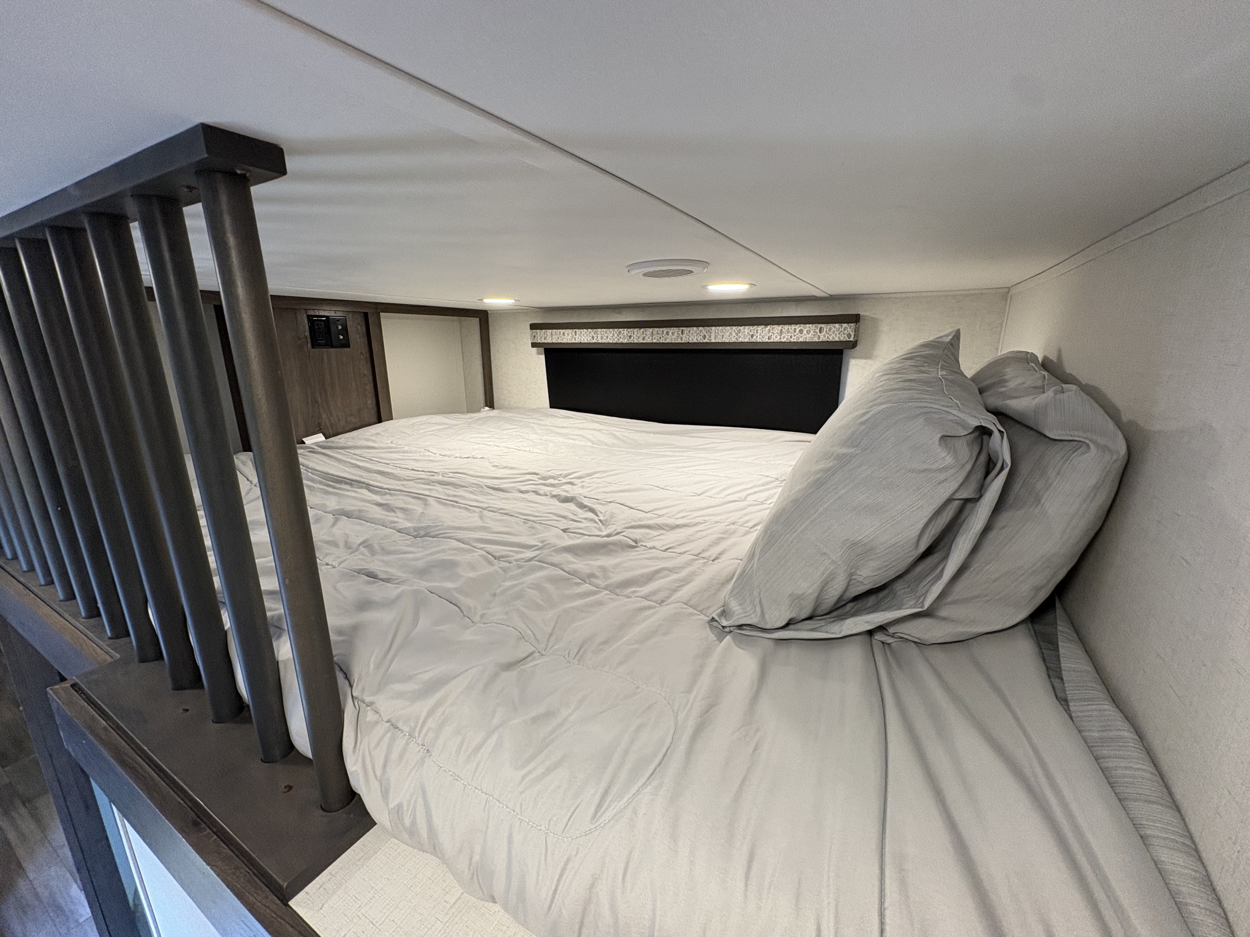 Cozy loft bed in an RV rental, featuring a soft gray comforter, pillows, and a dark safety railing, maximizing sleeping space.. Alliance RV Paradigm 2022