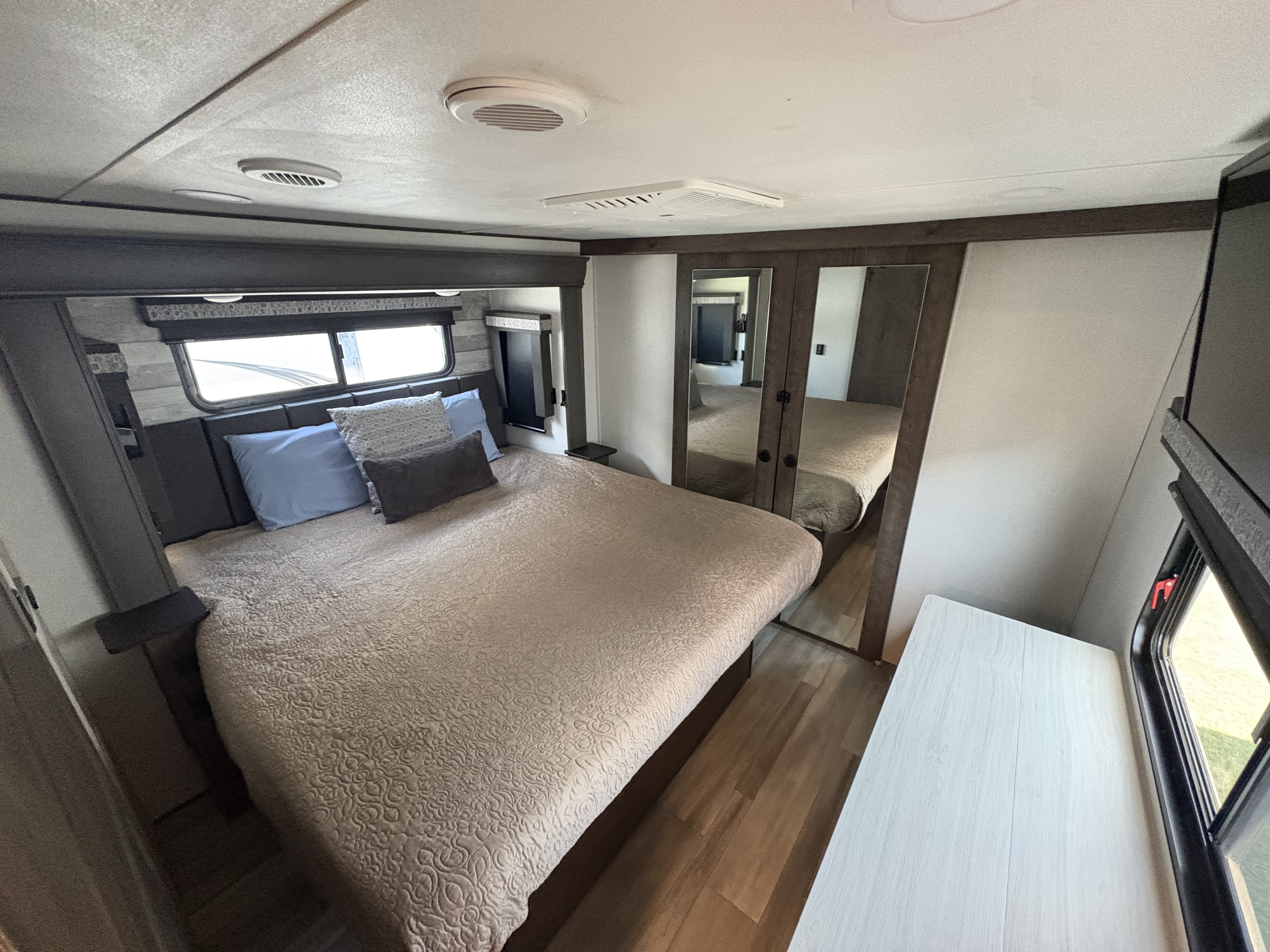 Comfortable RV rental bedroom with a large bed, mirrored closet, ceiling vents, and modern wood-look accents.. Alliance RV Paradigm 2022