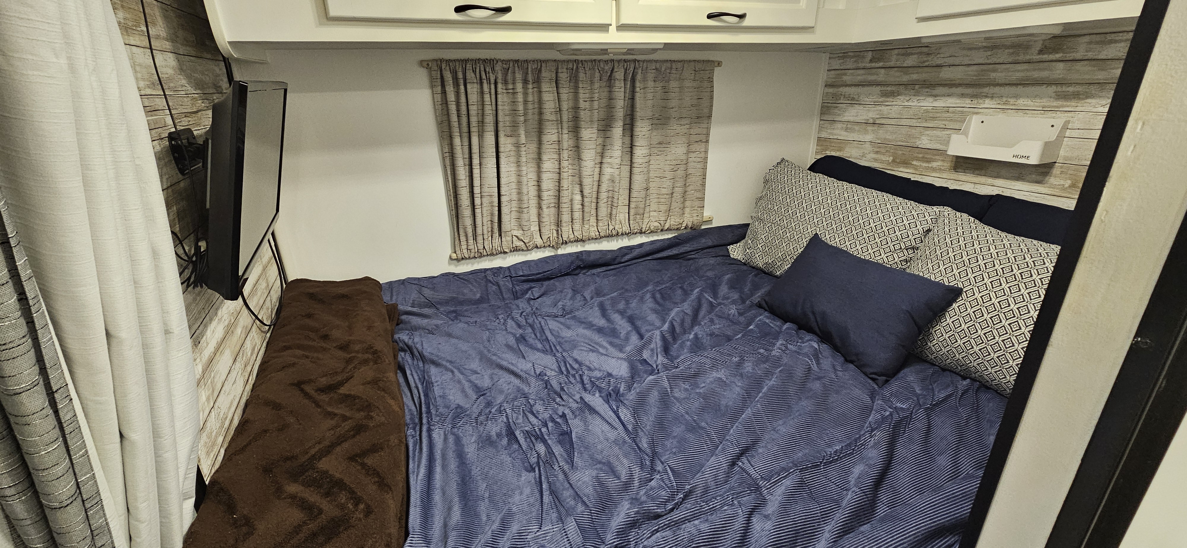 Experience comfort in this RV rental bedroom with blue striped bedding, a mounted TV, and charming wood-paneled walls.. Thor Majestic 2015