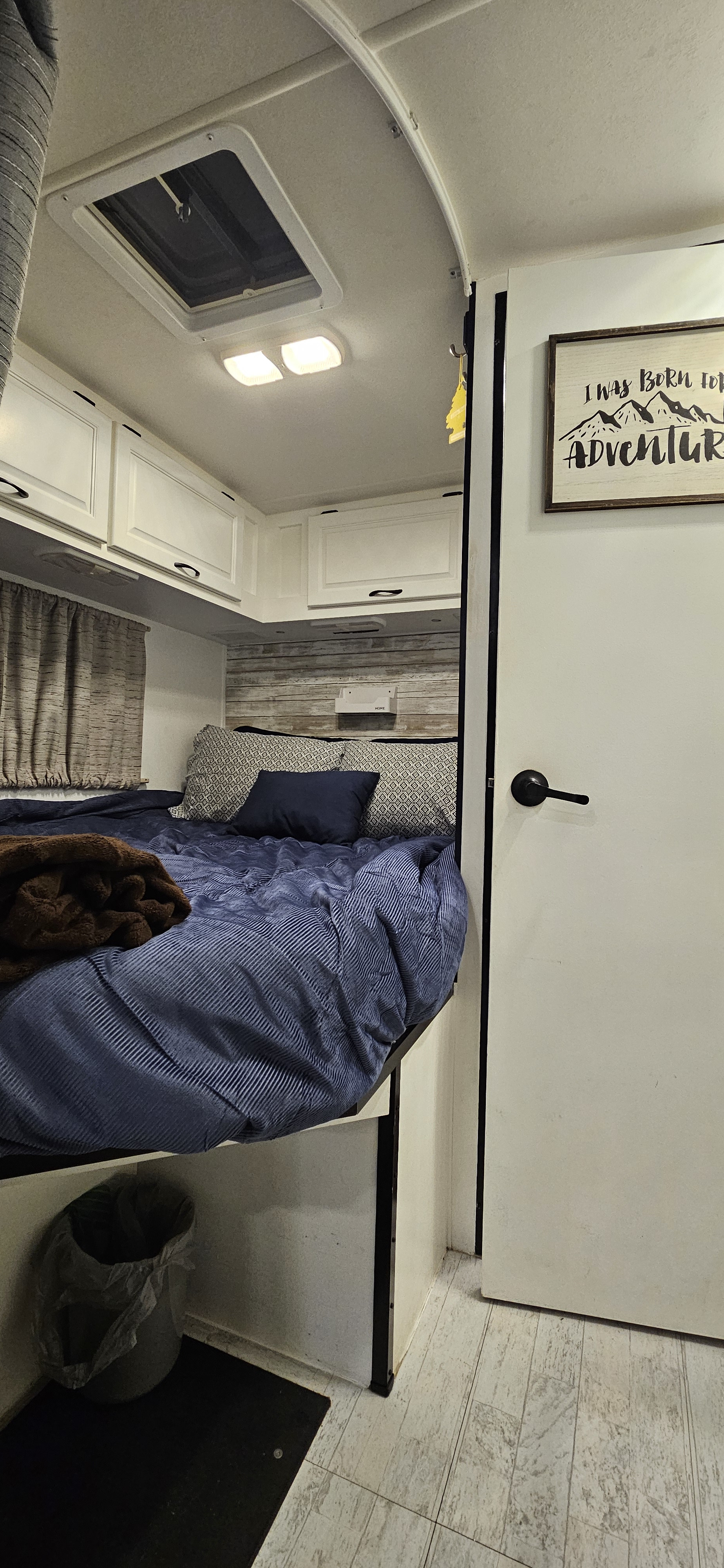 Inside a compact RV rental bedroom, featuring a comfy bed, skylight, and charming adventure sign.. Thor Majestic 2015