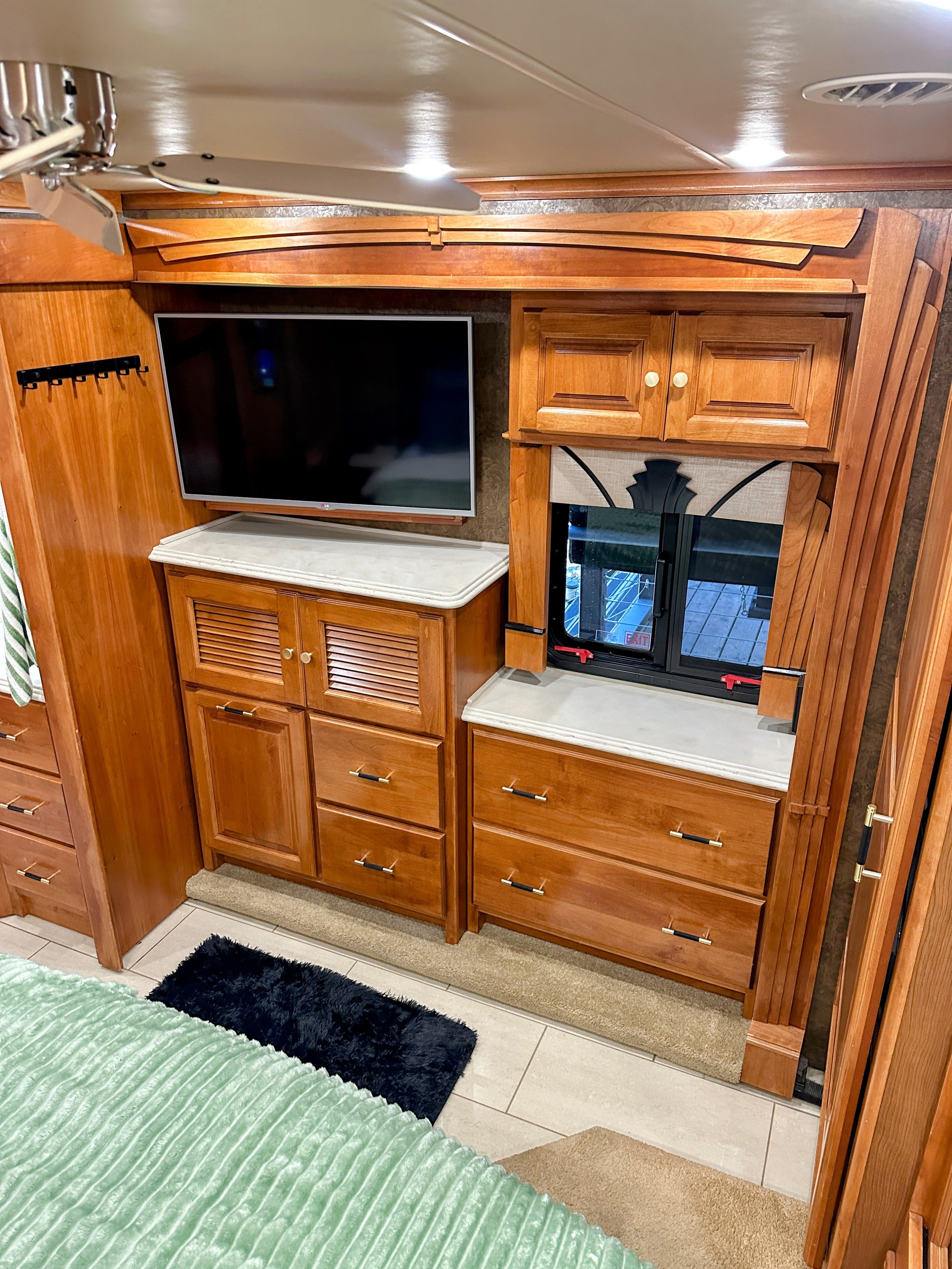 Modern RV rental bedroom interior featuring wood cabinetry, a TV, window, ceiling fan, and bed area.. Tiffin Phaeton 36 QHS 2015