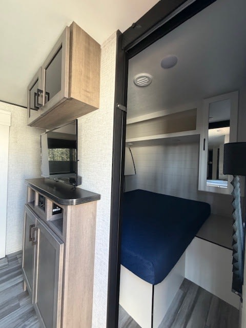 Cozy rv rental interior featuring a living area with TV and cabinets, plus a compact bedroom with a comfy blue mattress.. Jayco Jay Feather 2025