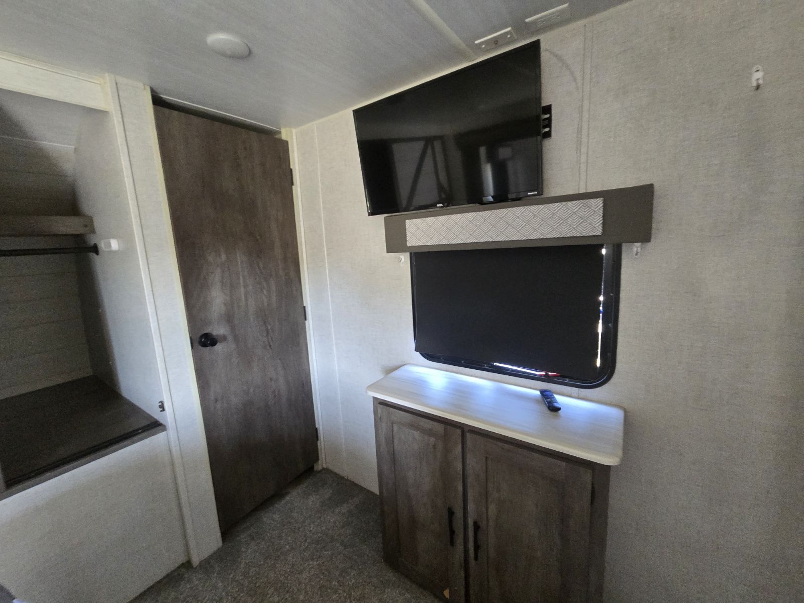 Wall-mounted TV in RV rental bedroom, with window over lit cabinet, a wooden door, and open closet space.. Salem 33TS 2020