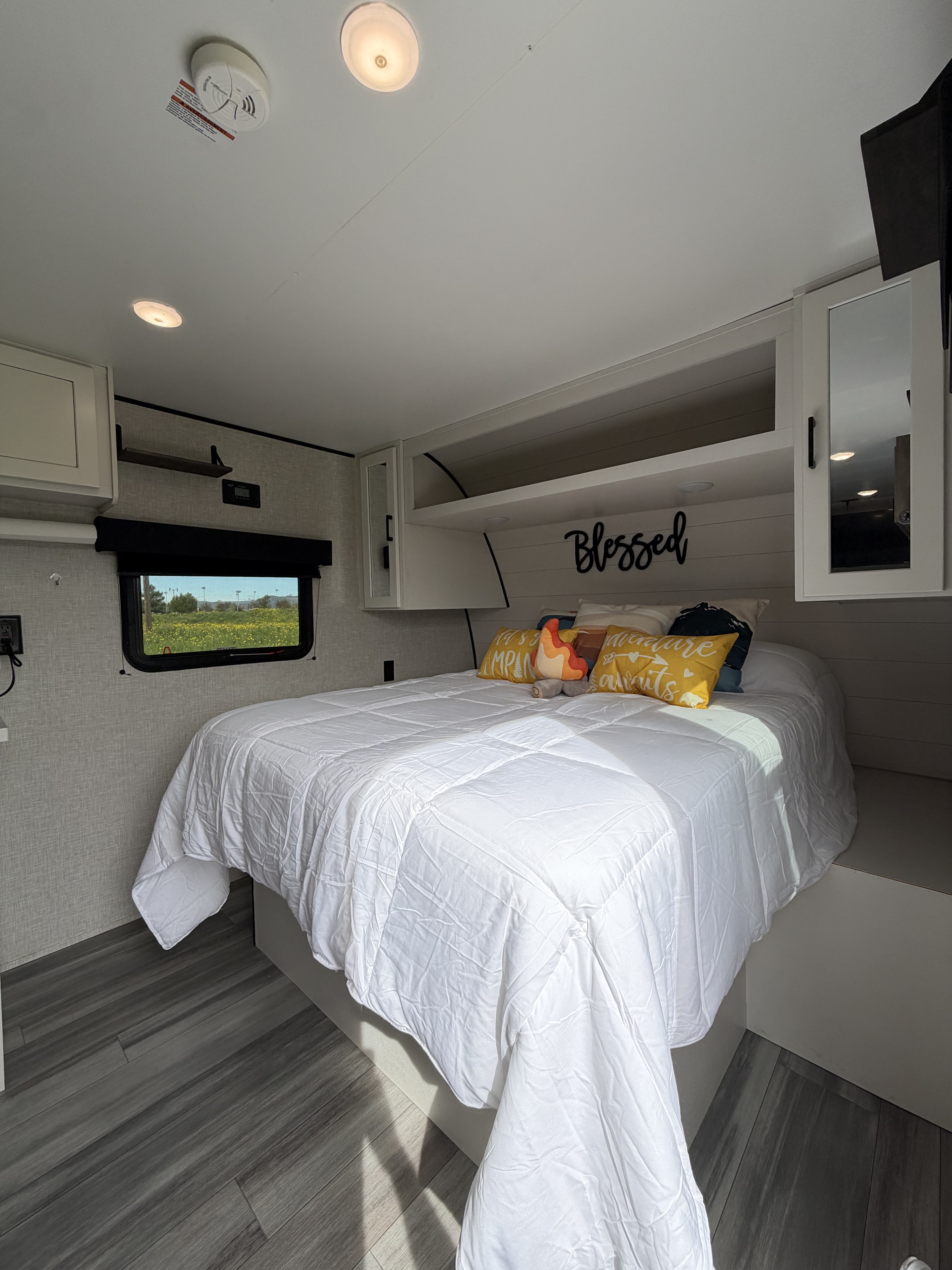 Cozy rv rental bedroom features a comfortable bed with colorful pillows, a window view, and overhead storage.. Jayco Jay Flight SLX Baja Edition 2025