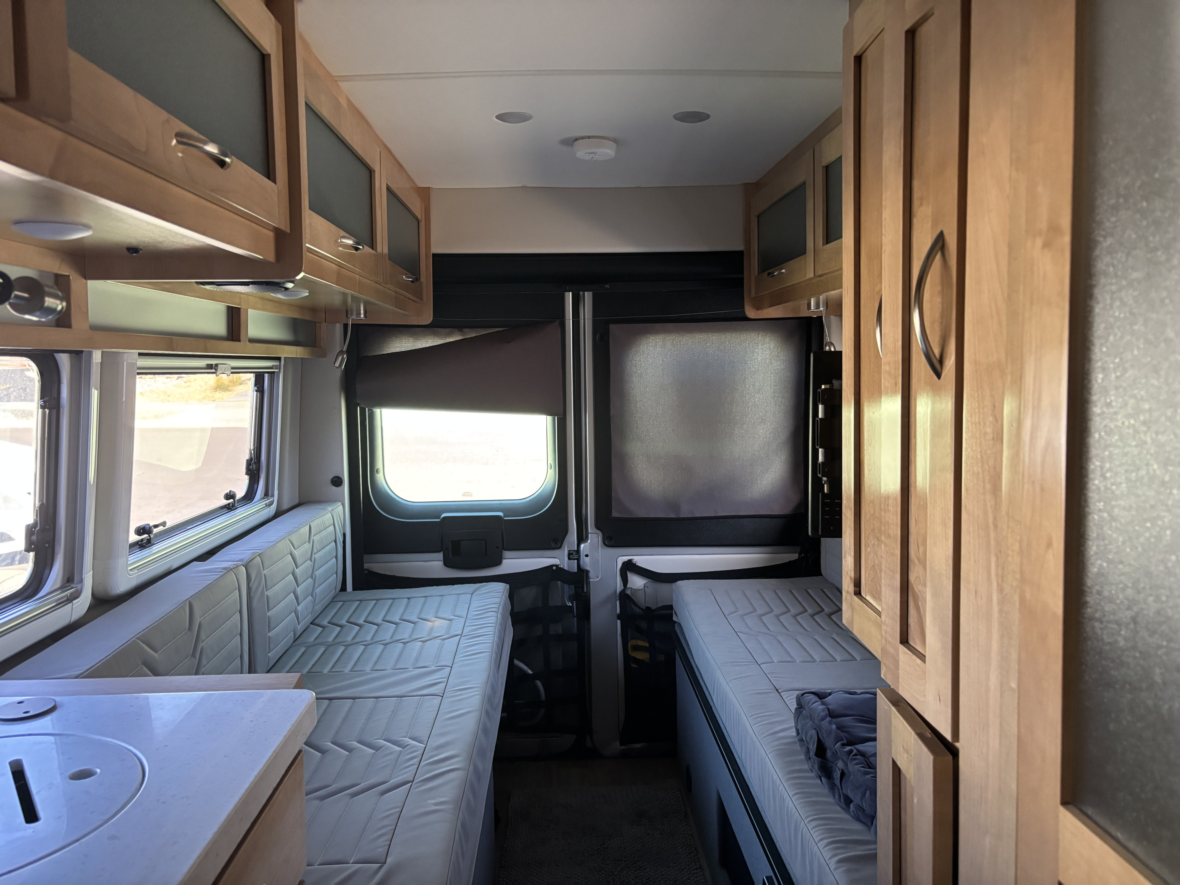 RV rental interior showcasing a cozy camper van with light wood cabinets, versatile seating/bed areas, and a small kitchen prep space.. Coachmen NOVA 20D 2024