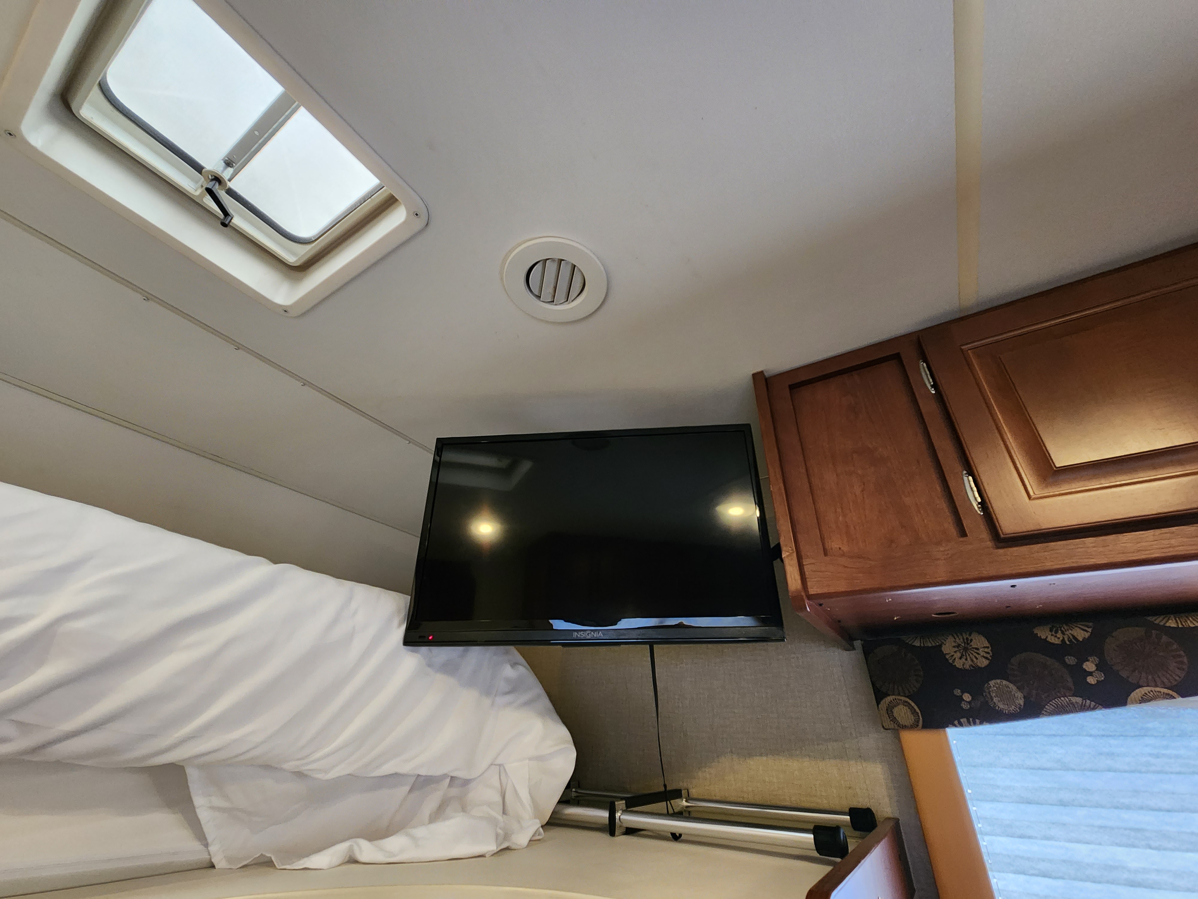 RV rental interior: A cozy view of the bed, TV, skylight, and wooden cabinets, highlighting comfort and features.. Winnebago Minnie Winnie 2015