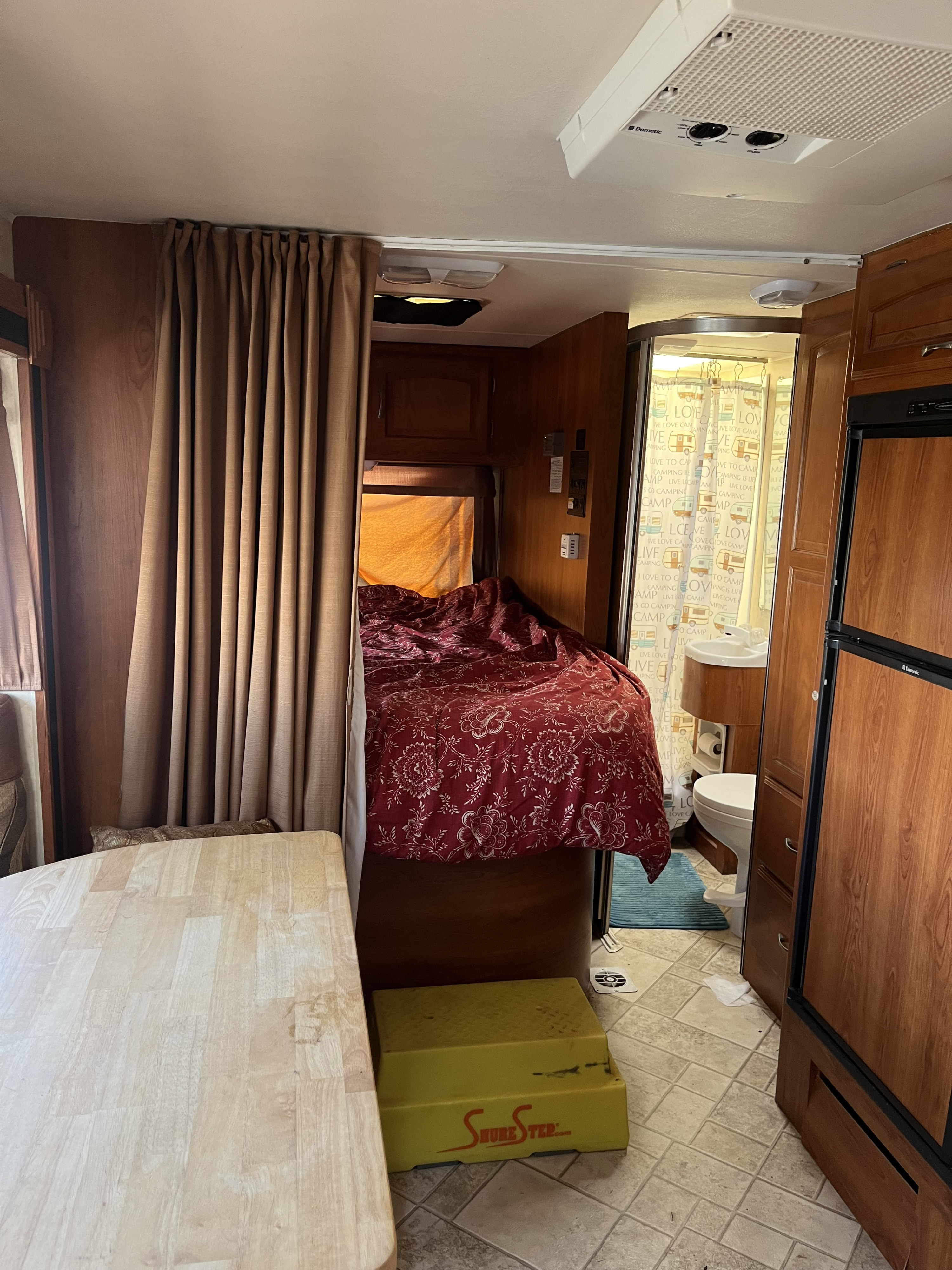 Cozy RV rental interior featuring a compact bedroom with a red comforter, bathroom with a sink, and a Dometic fridge.. Forest River Coachmen Freelander 2011