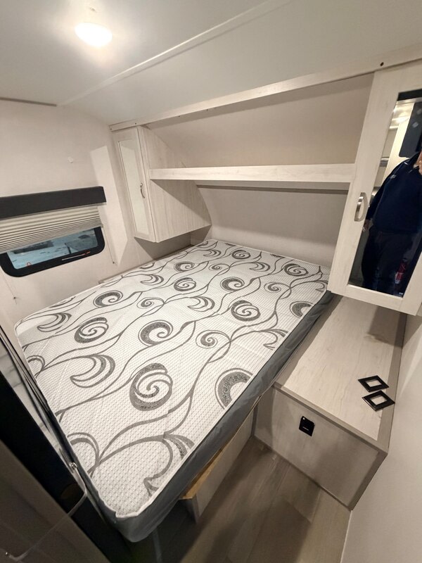 Cozy RV rental bedroom featuring a patterned mattress, overhead shelves, a mirrored cabinet, and a window for comfortable travel.. Forest River Tracer 2022