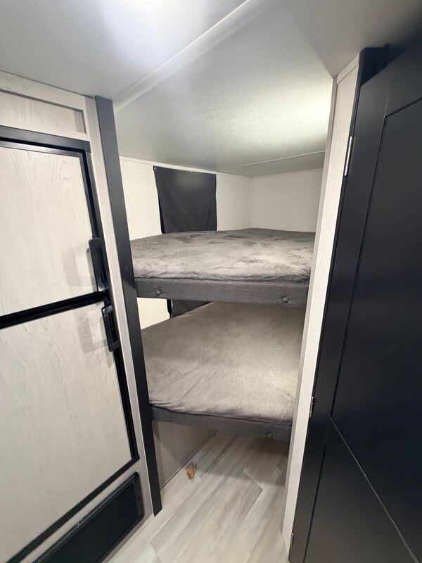RV rental bunk room: Two cozy beds with grey blankets, flanked by light and dark cabinetry, ideal for family travel.. Forest River Tracer 2022