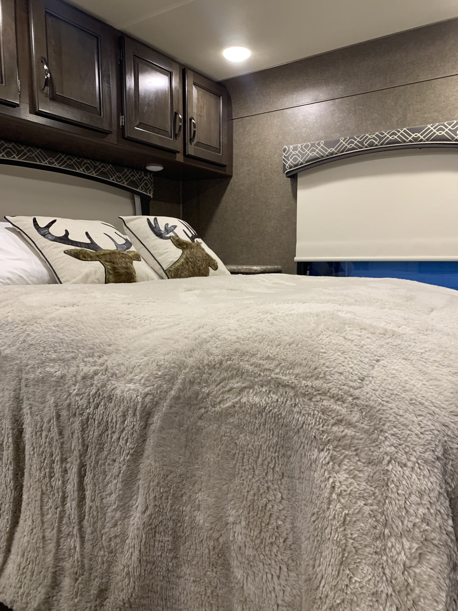 Enjoy a cozy night in this RV rental bedroom featuring fluffy bedding, deer pillows, and overhead cabinets.. Thor Chateau 2020