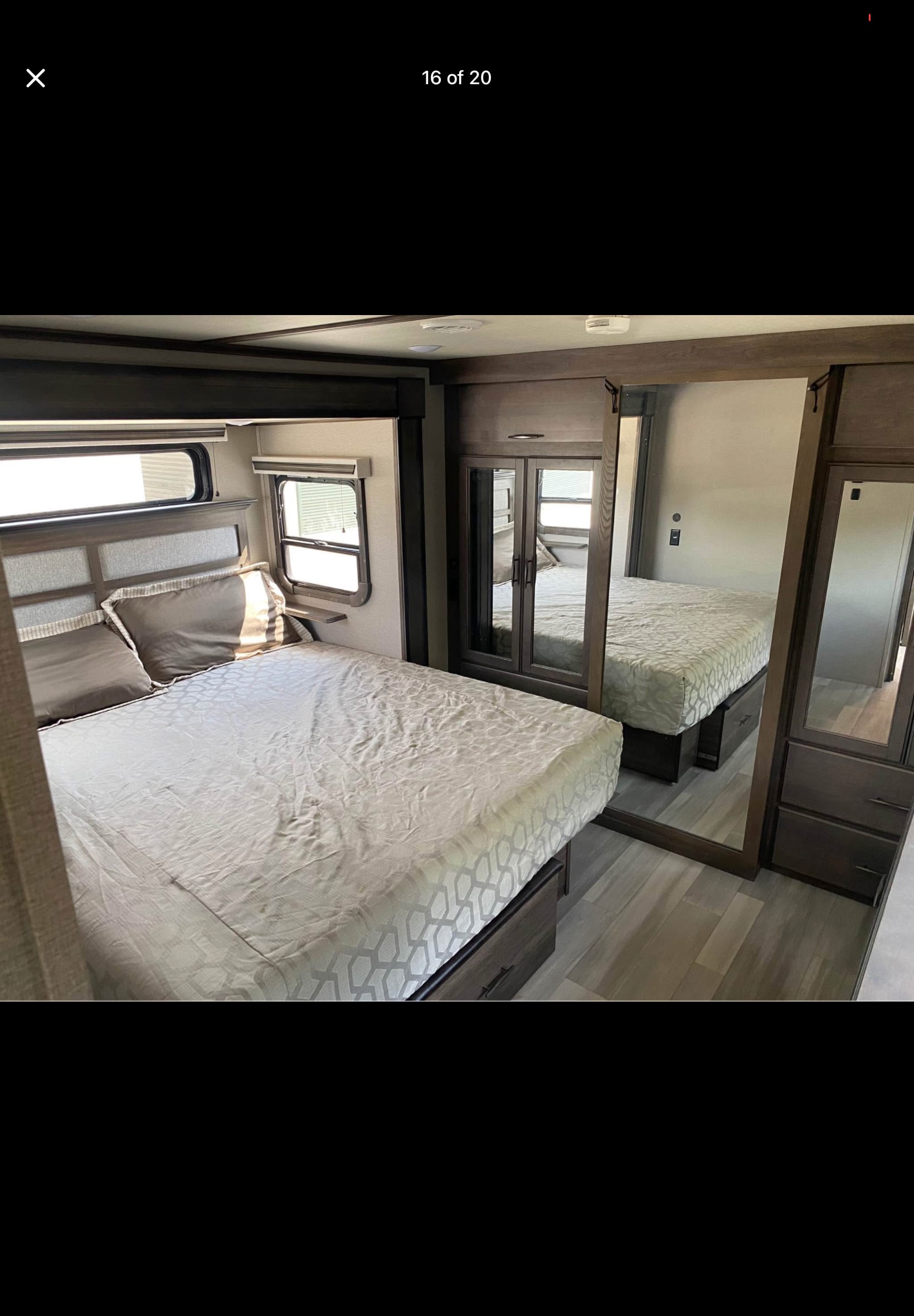 Bright rv rental bedroom featuring a patterned bed, dark wood accents, windows, and mirrored wardrobes.. Grand Design Solitude 390RK-R 2023