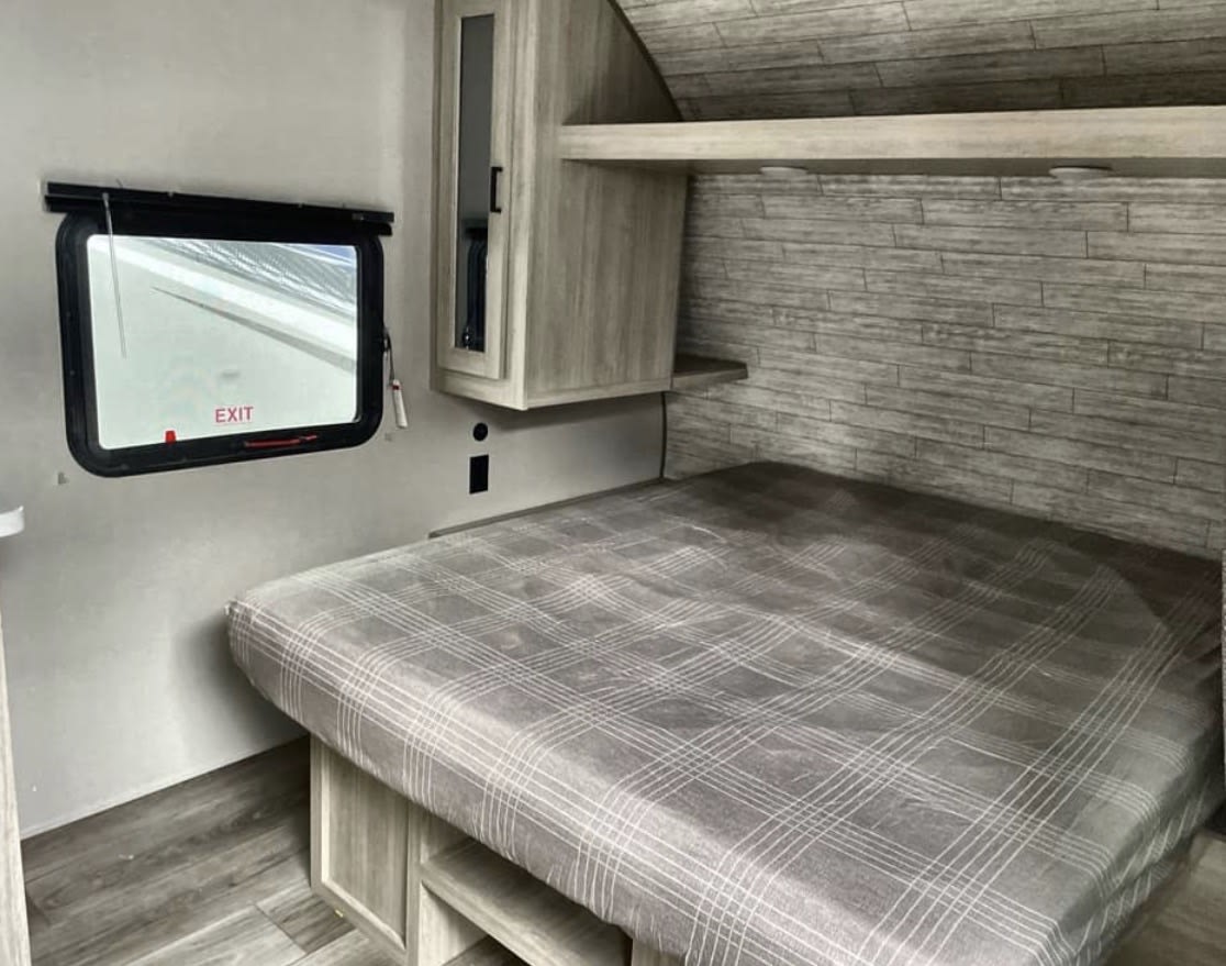 Cozy RV rental bedroom features a comfortable plaid bed, emergency exit window, and ample storage. Perfect for travel.. Coachmen CATALINA SUMMIT 211BH 2026