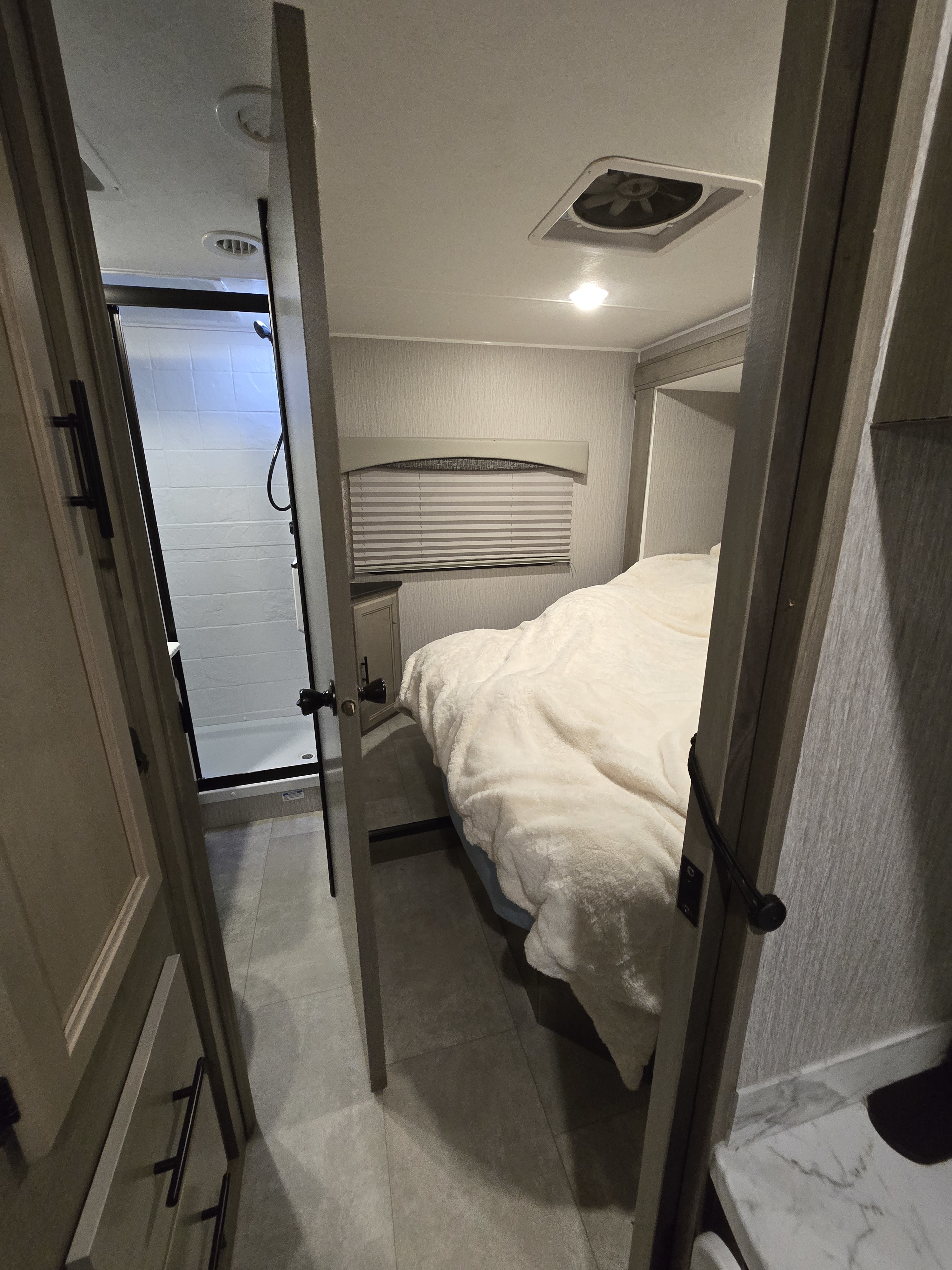 Cozy RV rental interior featuring a bedroom with fluffy bed, window blinds, and a shower bathroom visible through an open door.. Ford Coachmen Freelander Ford Coachmen Freelander 2023