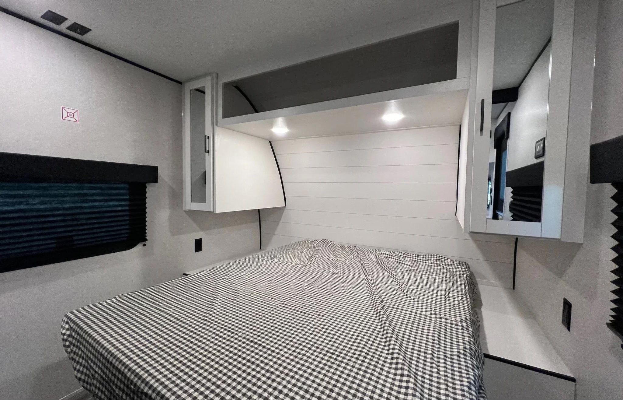 Cozy RV rental bedroom: black/white gingham bed, white shiplap wall, overhead cabinets, and bright lights for comfort.. Jayco Jay Flight SLX 2026