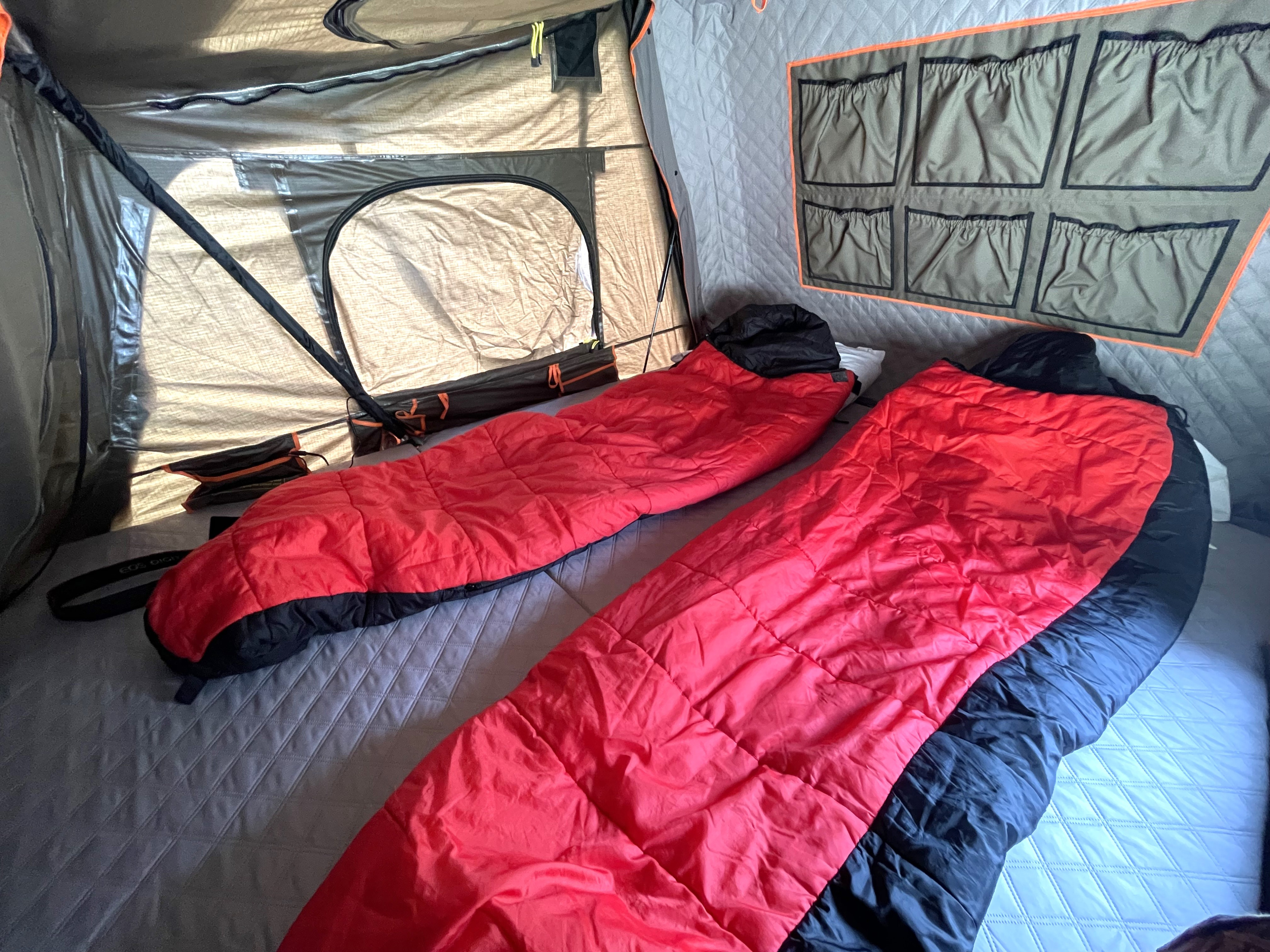 Inside a spacious RV rental: two red sleeping bags on a quilted bed, wall storage, and windows, ready for your camping travel.. Jeep Wrangler Unlimited 2020