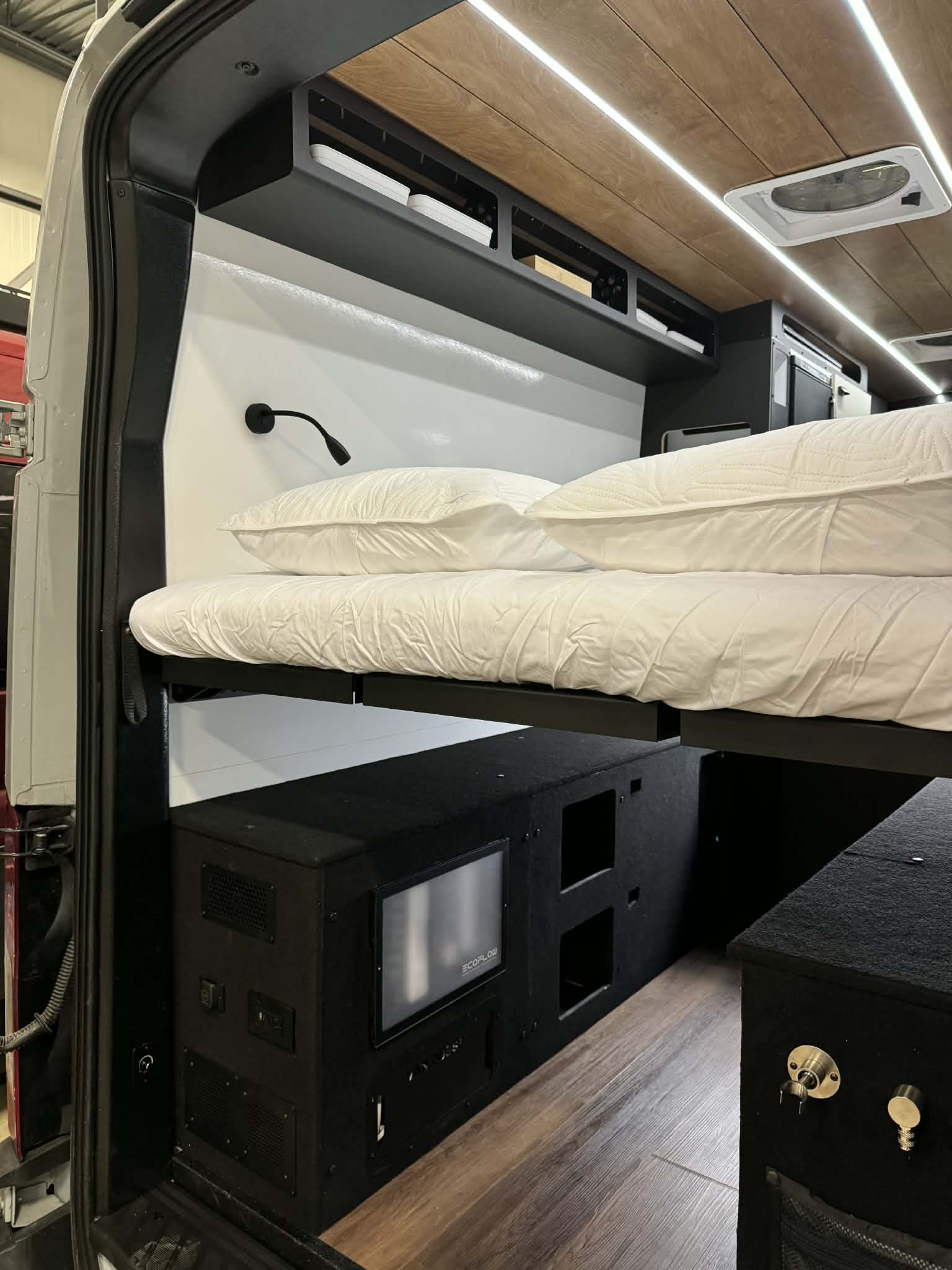 Explore this RV rental's van conversion: a comfy bed above an EcoFlow power unit & storage. LED lighting accents wood ceiling.. Ford Transit 250 2025