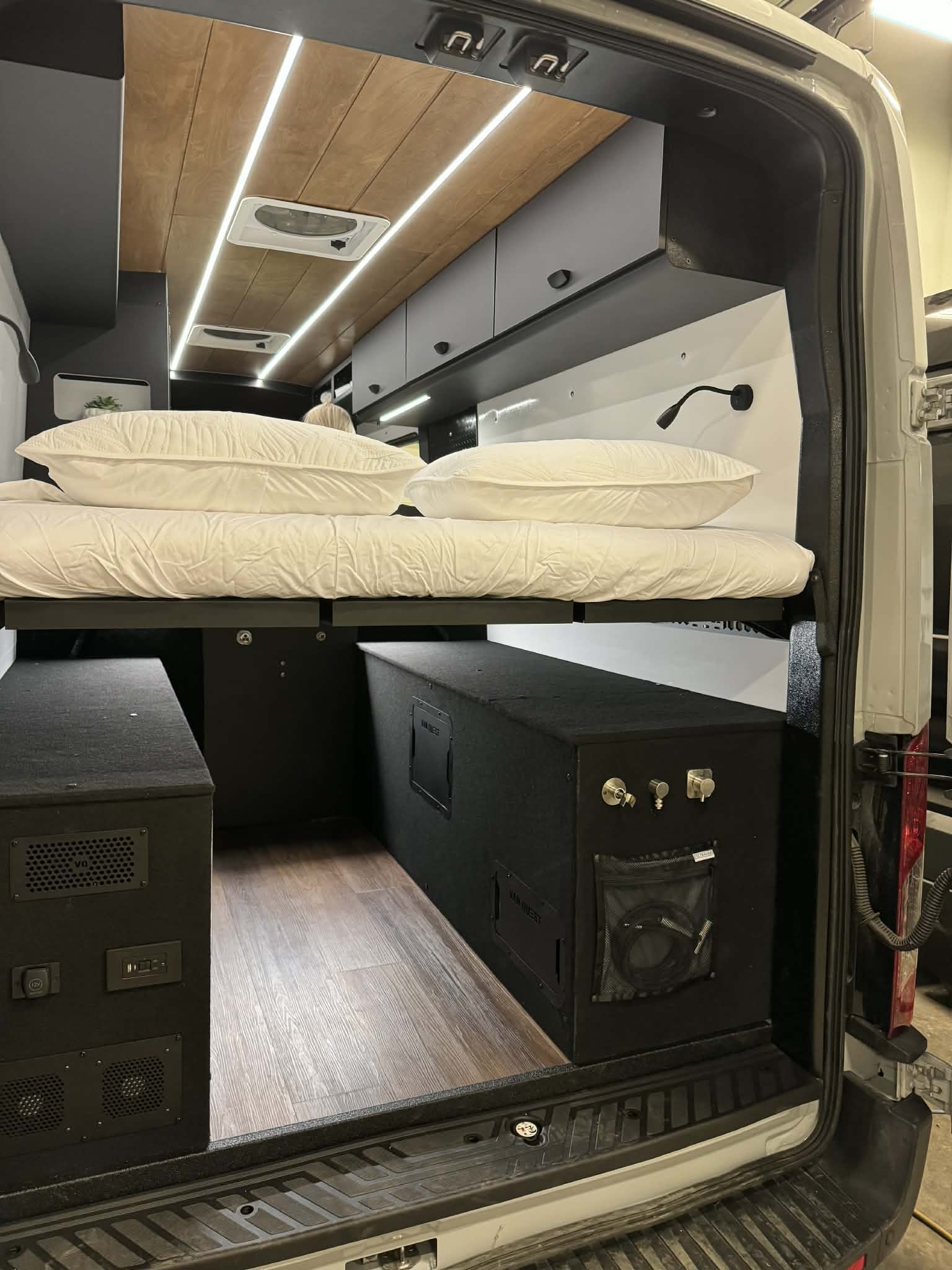 This RV rental features a modern van conversion with a high bed over storage, wood-paneled ceiling with LEDs, and wood flooring.. Ford Transit 250 2025