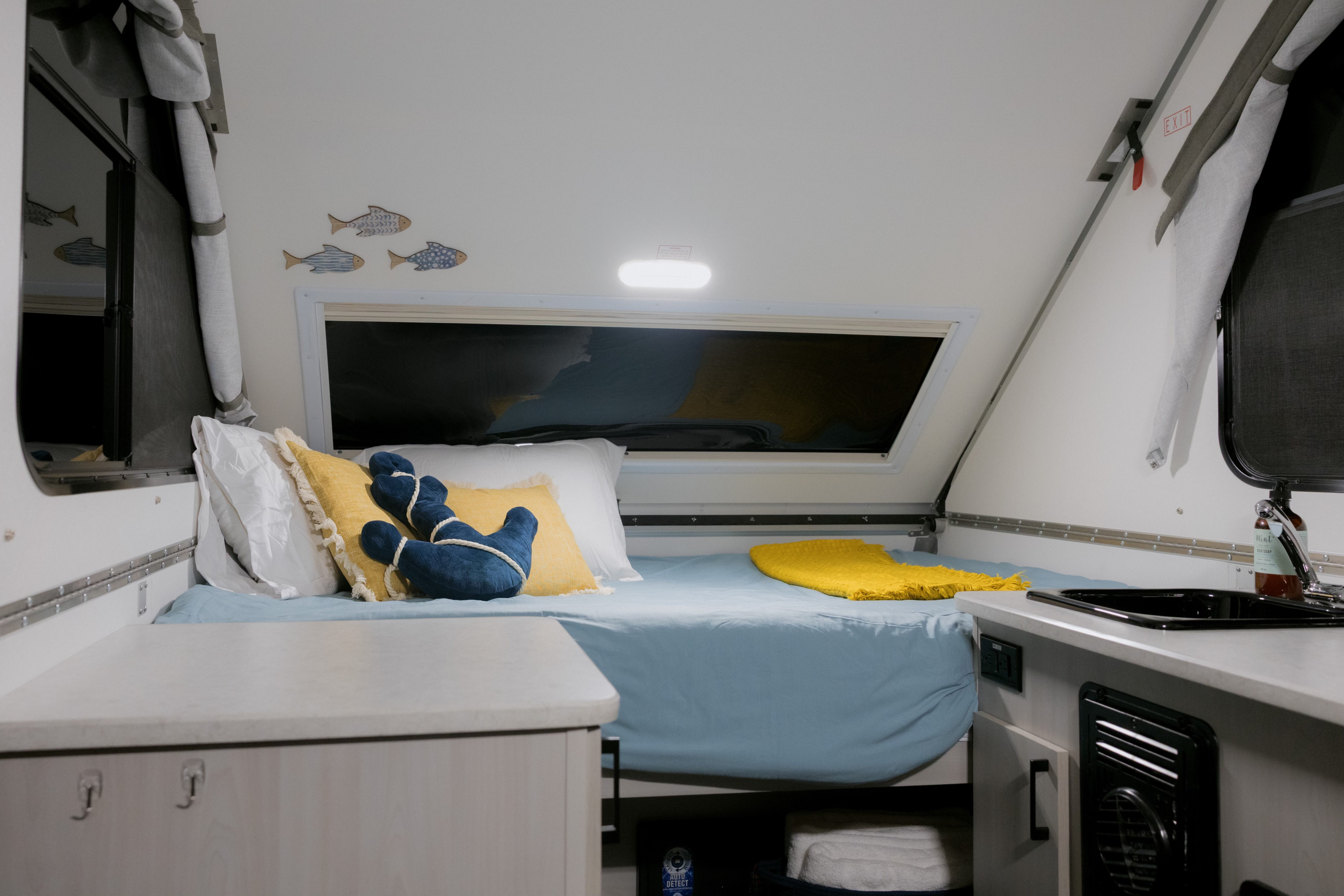 Compact RV rental interior featuring a cozy bed with blue linens, nautical decor, and a small kitchenette sink.. A Liner Scout 2026
