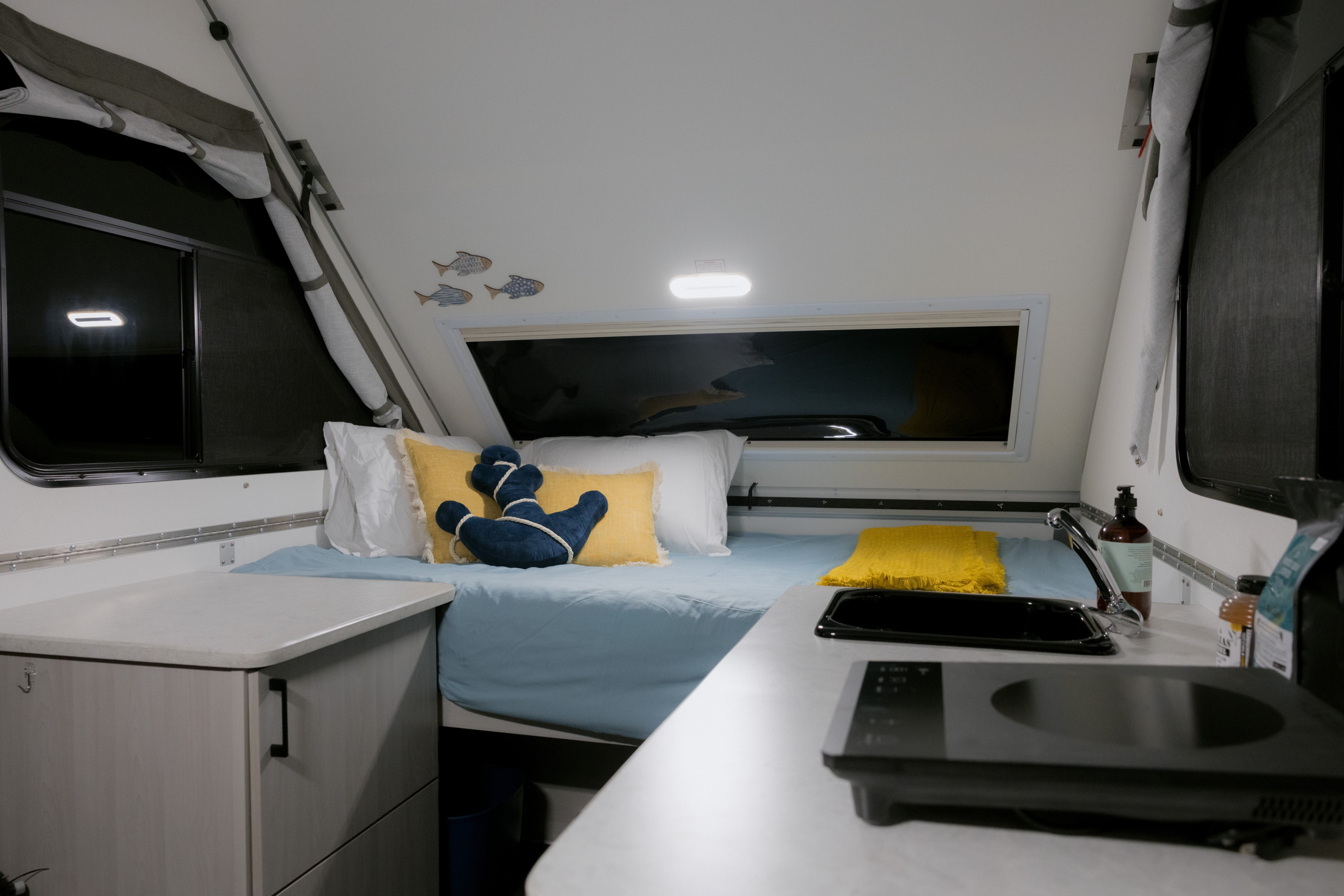 Cozy A-frame RV rental interior with a light blue bed, nautical decor, and a compact kitchen counter, sink, and cooktop.. A Liner Scout 2026