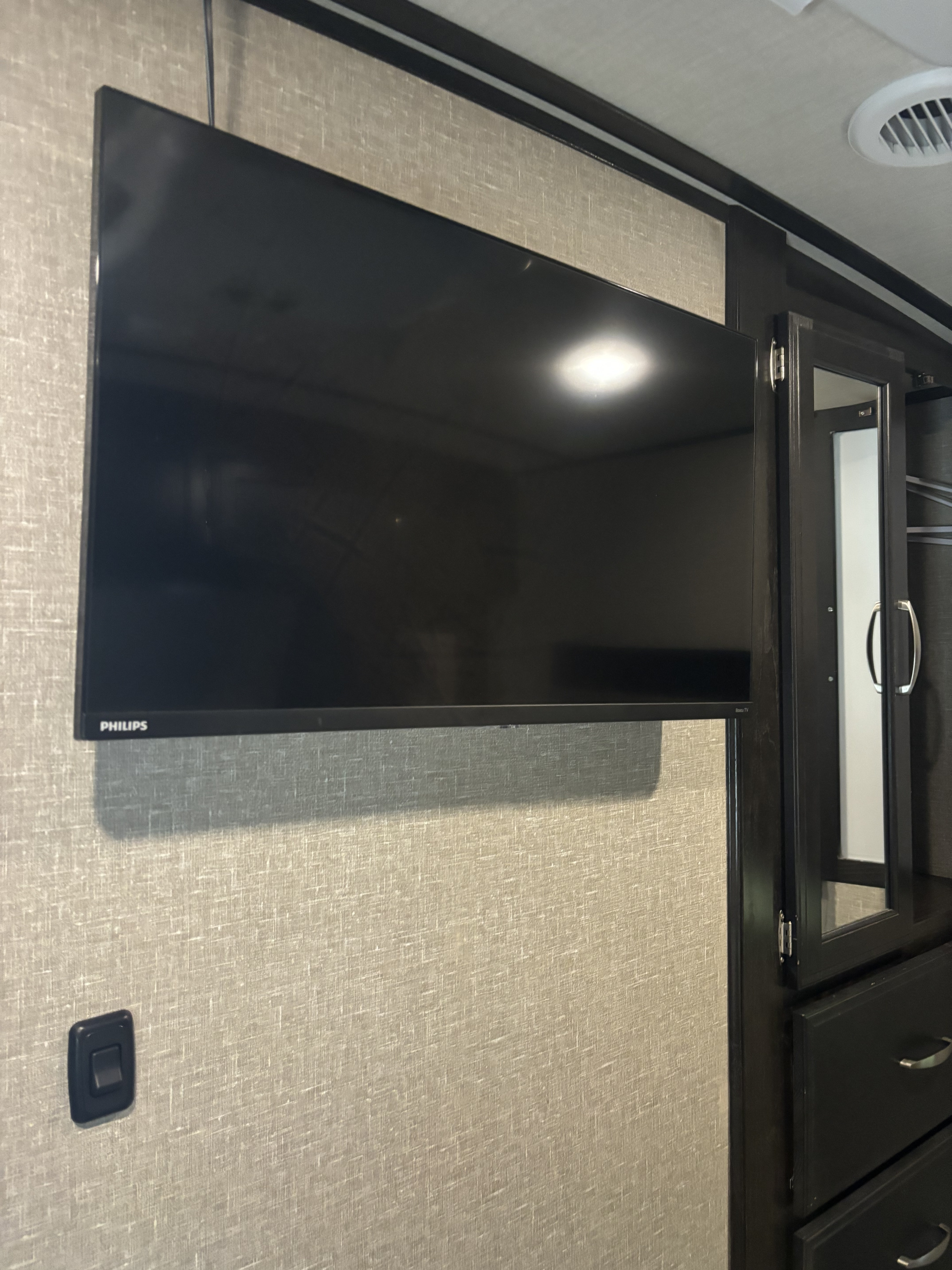 RV rental interior showcasing a wall-mounted Philips TV, stylish textured wall, and dark wood cabinet with mirrored door and drawers.. Grand Design Imagine 2019