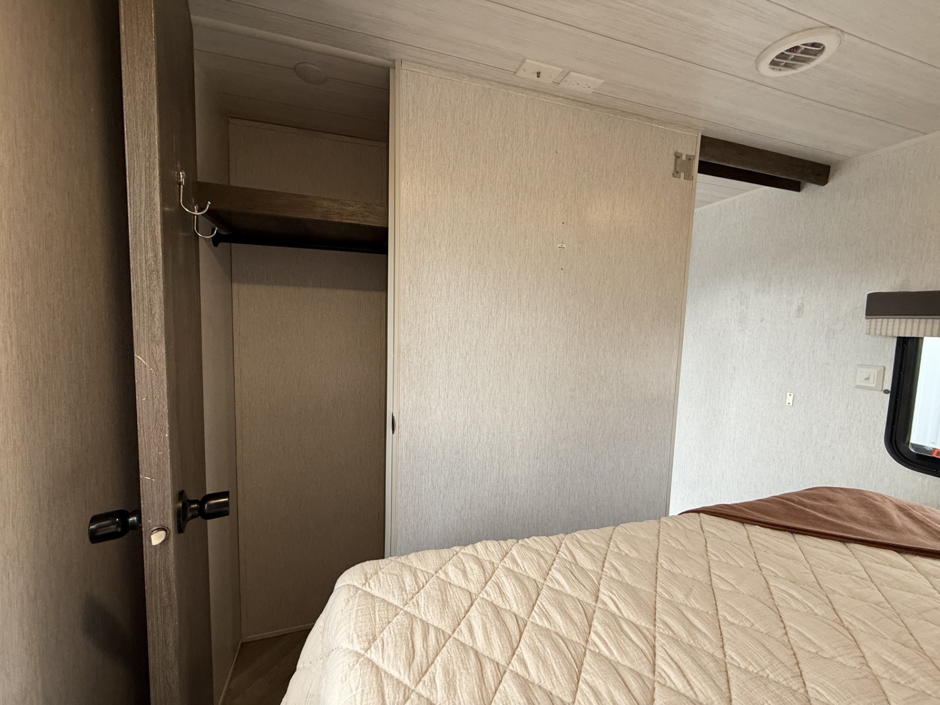 Cozy RV rental bedroom with a comfortable bed, open closet featuring a hanging rod and hooks, plus a sliding door and window.. Forest River Salem 2022