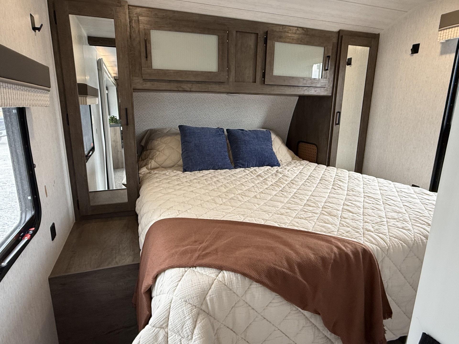 Cozy RV rental bedroom with a comfy bed, blue pillows, overhead storage, mirrored closets, and a side window.. Forest River Salem 2022