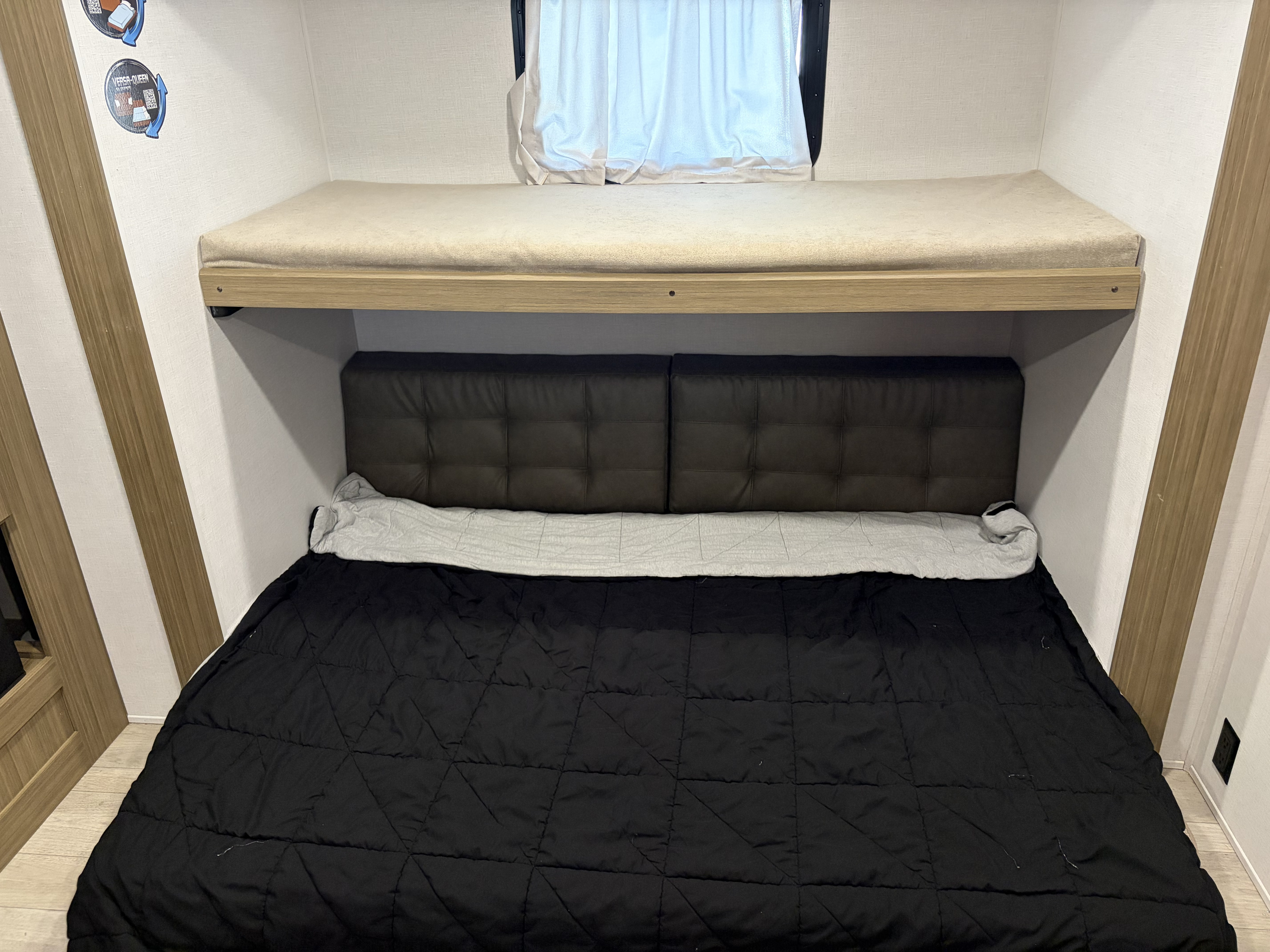 RV rental interior features cozy bunk beds. Top bunk has a light mattress; lower bed offers a dark comforter & tufted headboard.. Forest River Wildwood 2025