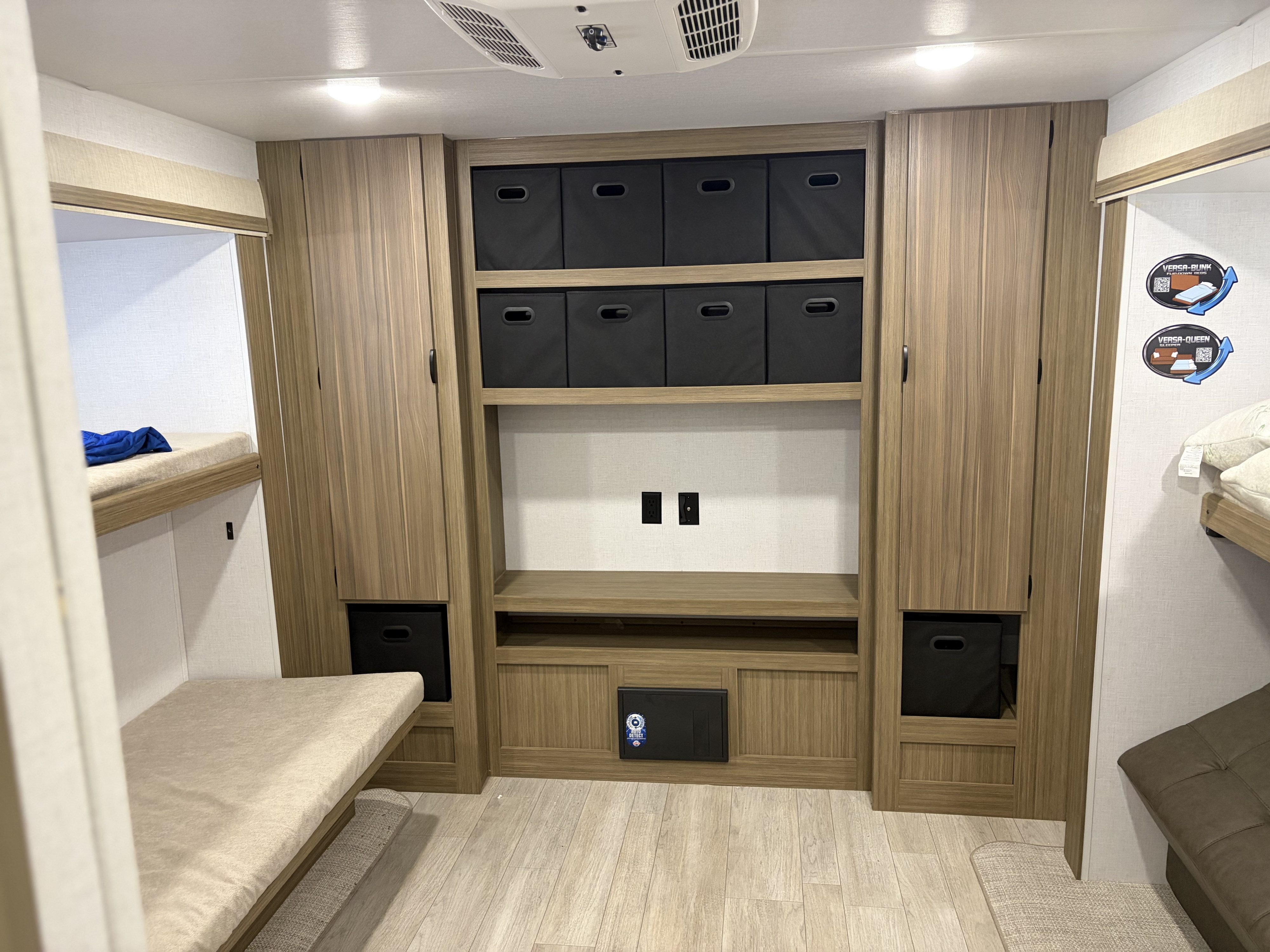 RV rental interior: bunk beds frame a central unit with light wood storage, black bins, and media outlets.. Forest River Wildwood 2025
