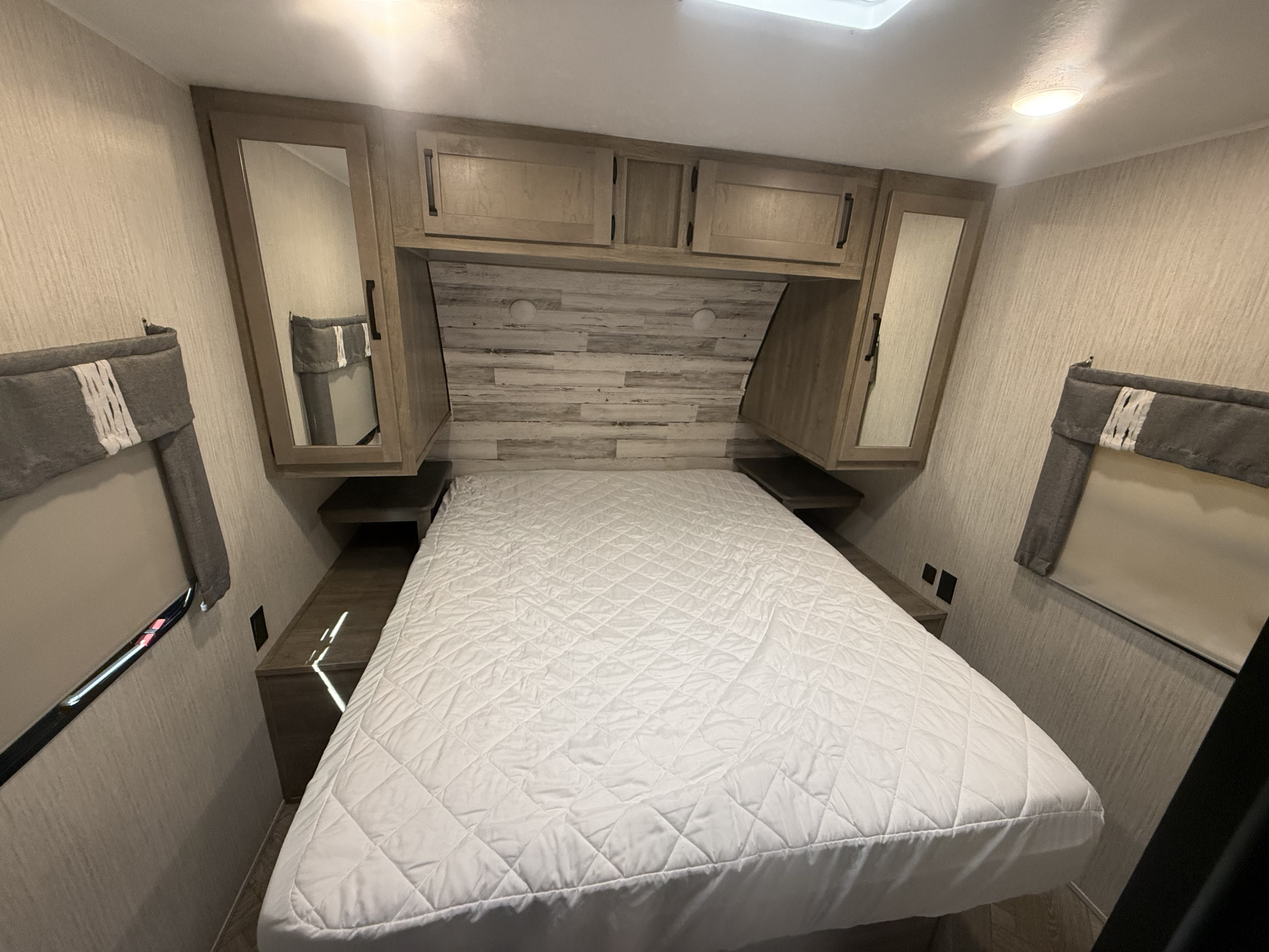 Cozy RV rental bedroom with a quilted bed, overhead cabinets, and mirrored wardrobes for a comfortable stay.. Forest River Palomino Puma 2022