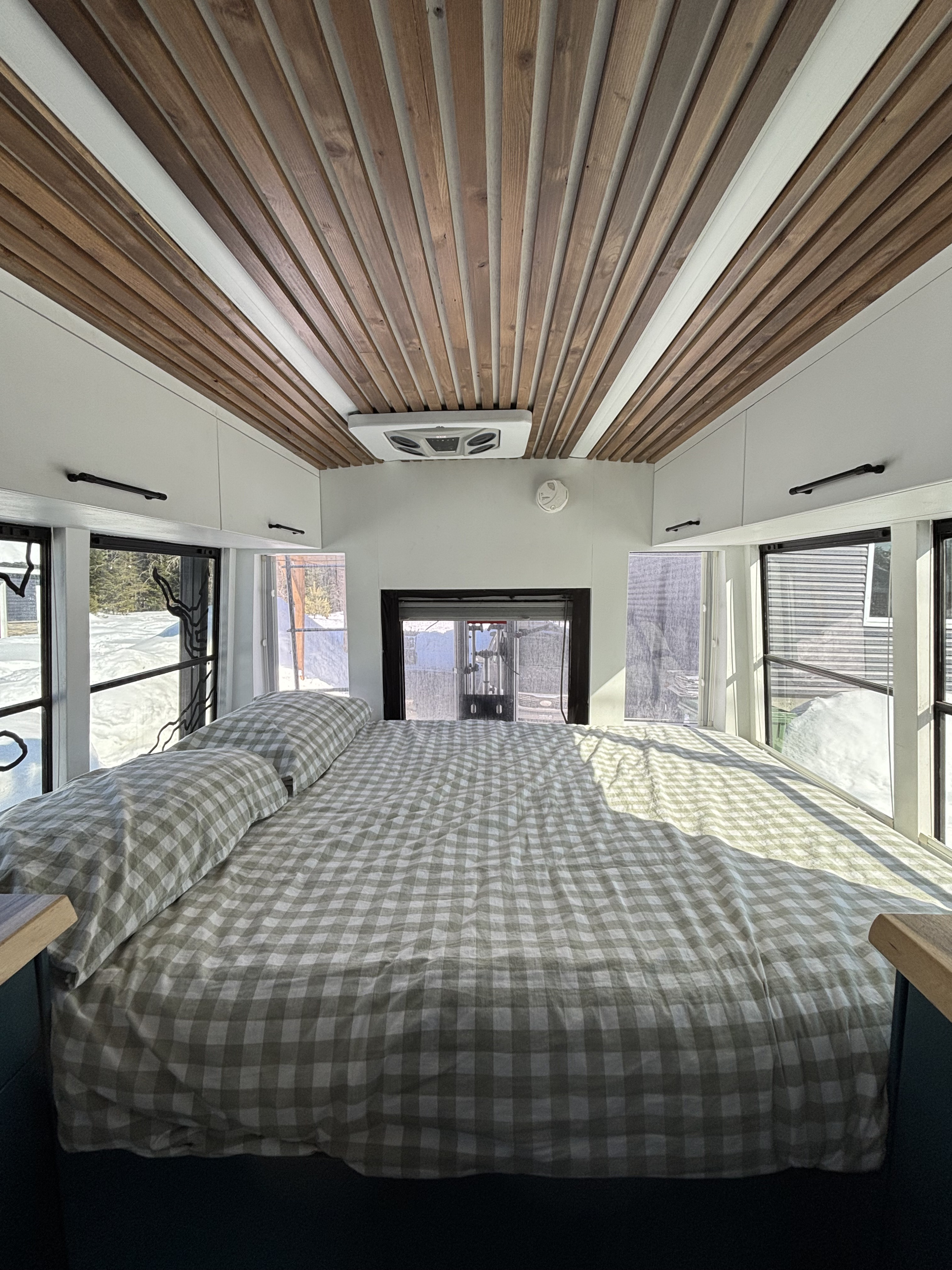 Cozy RV rental bedroom featuring gingham bedding, a stylish wooden slatted ceiling, and bright snowy views from the large windows.. Ford E450 2006
