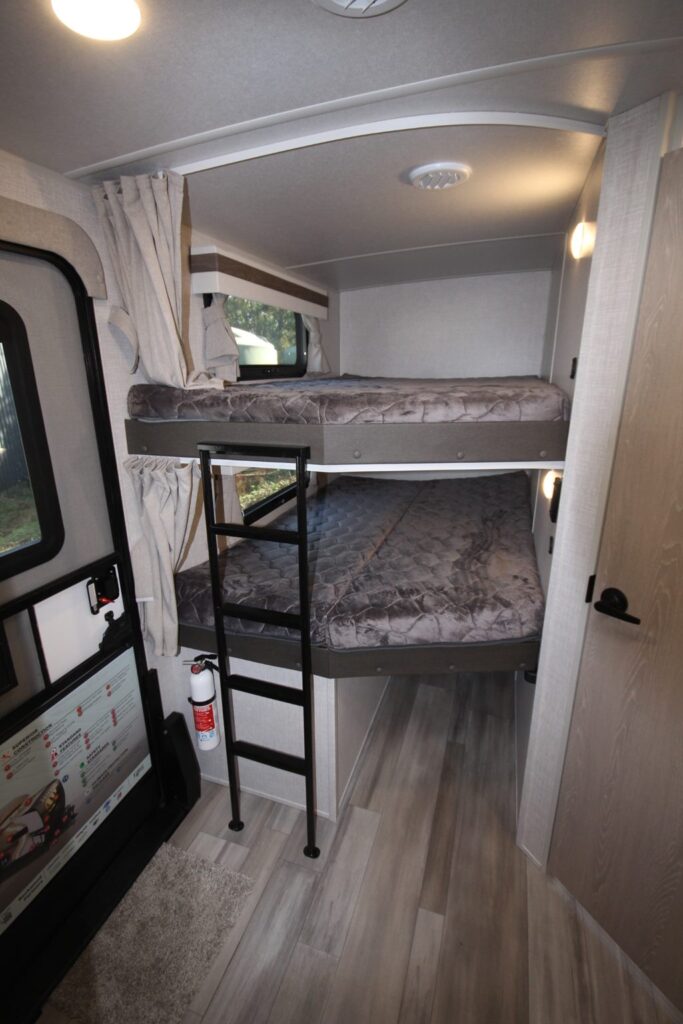 RV rental interior: two cozy bunk beds with a ladder, window with curtains, and fire extinguisher for safety.. Forest River Rockwood Ultra Lite 2024