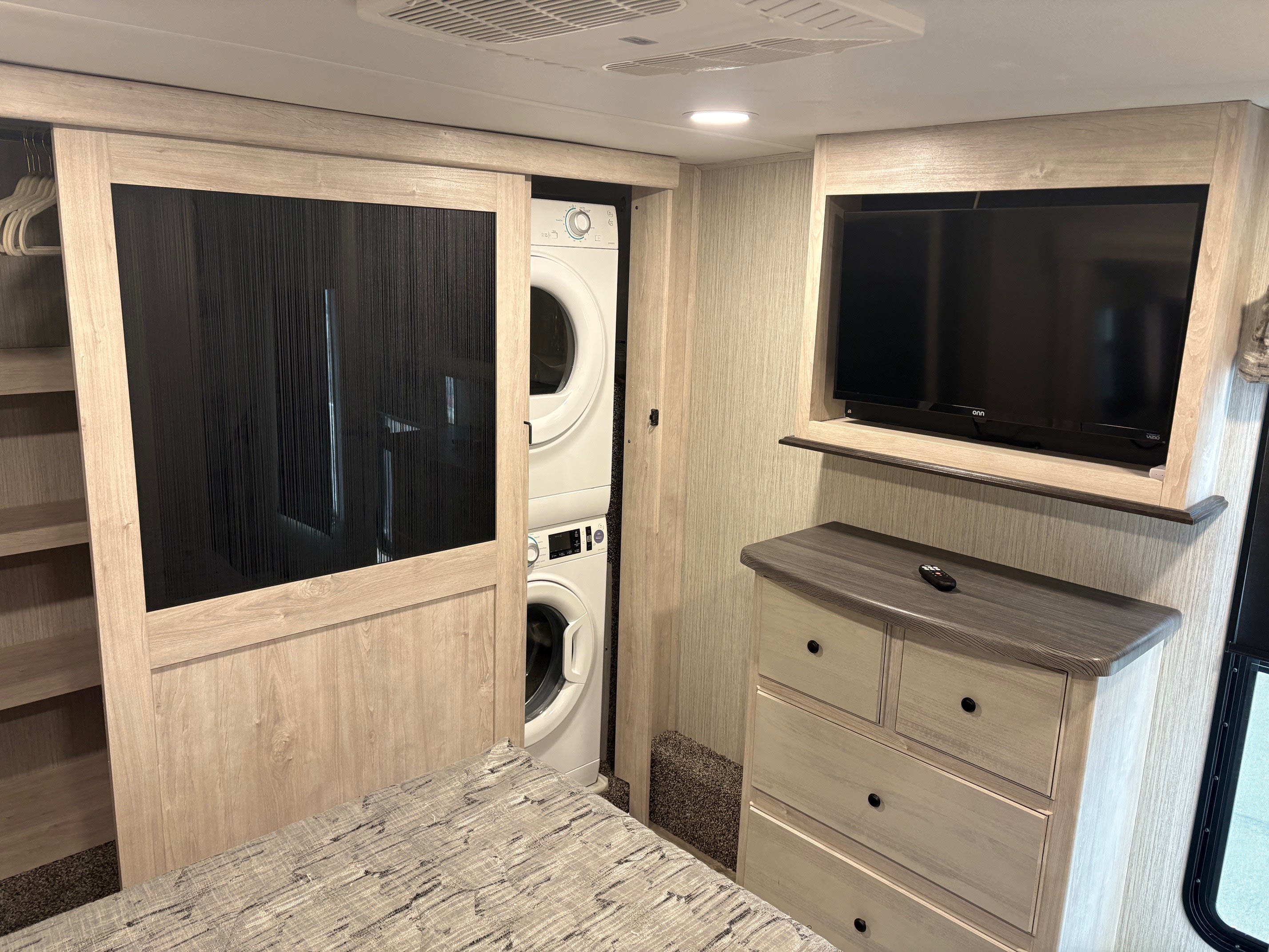 This RV rental bedroom features a built-in dresser with TV, sliding closet, and stacked washer/dryer for convenience.. Forest River Sandpiper 2022
