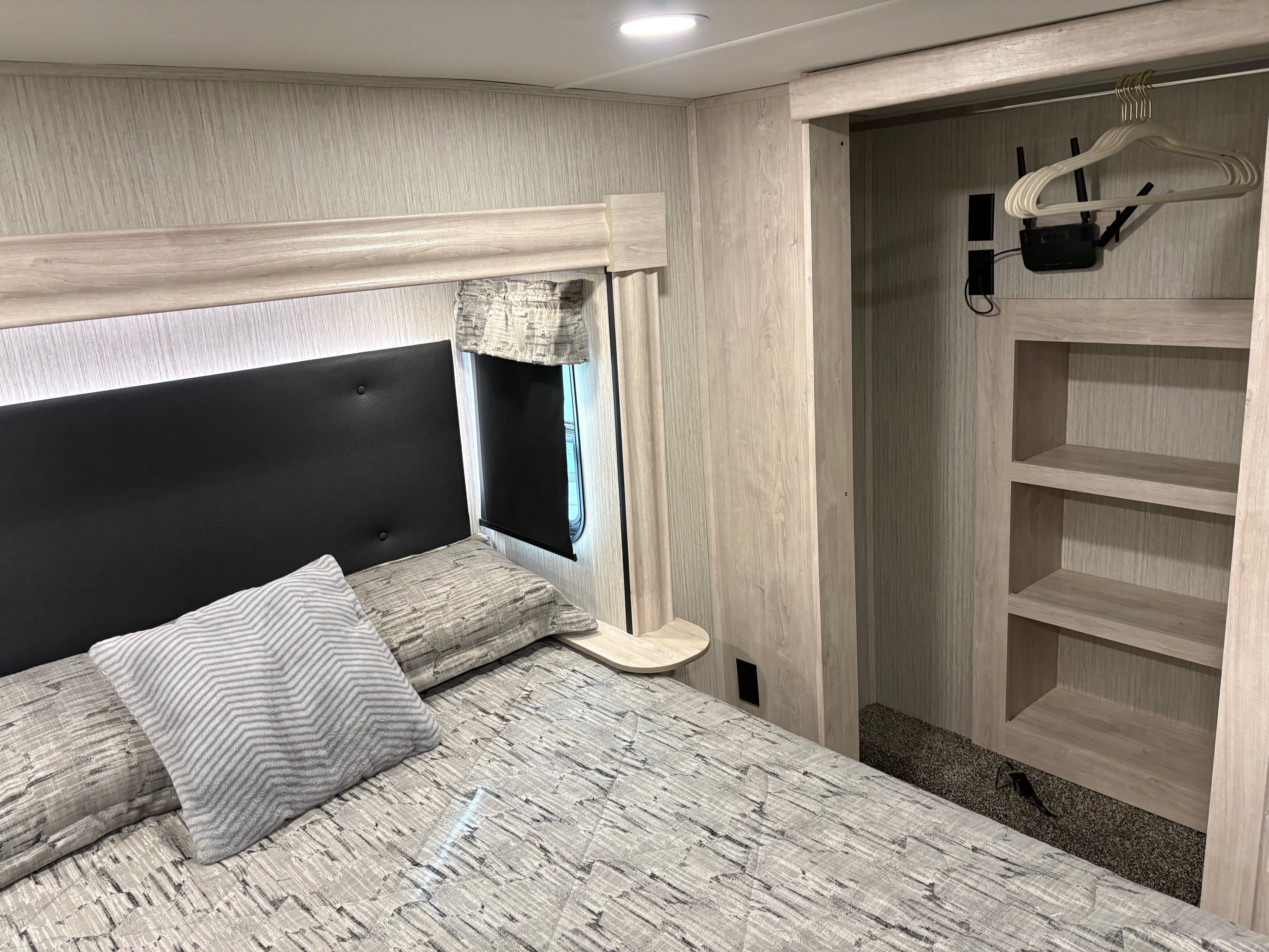 Bright RV rental bedroom showcasing a bed with neutral linens, a modern headboard, and an open closet with shelves.. Forest River Sandpiper 2022