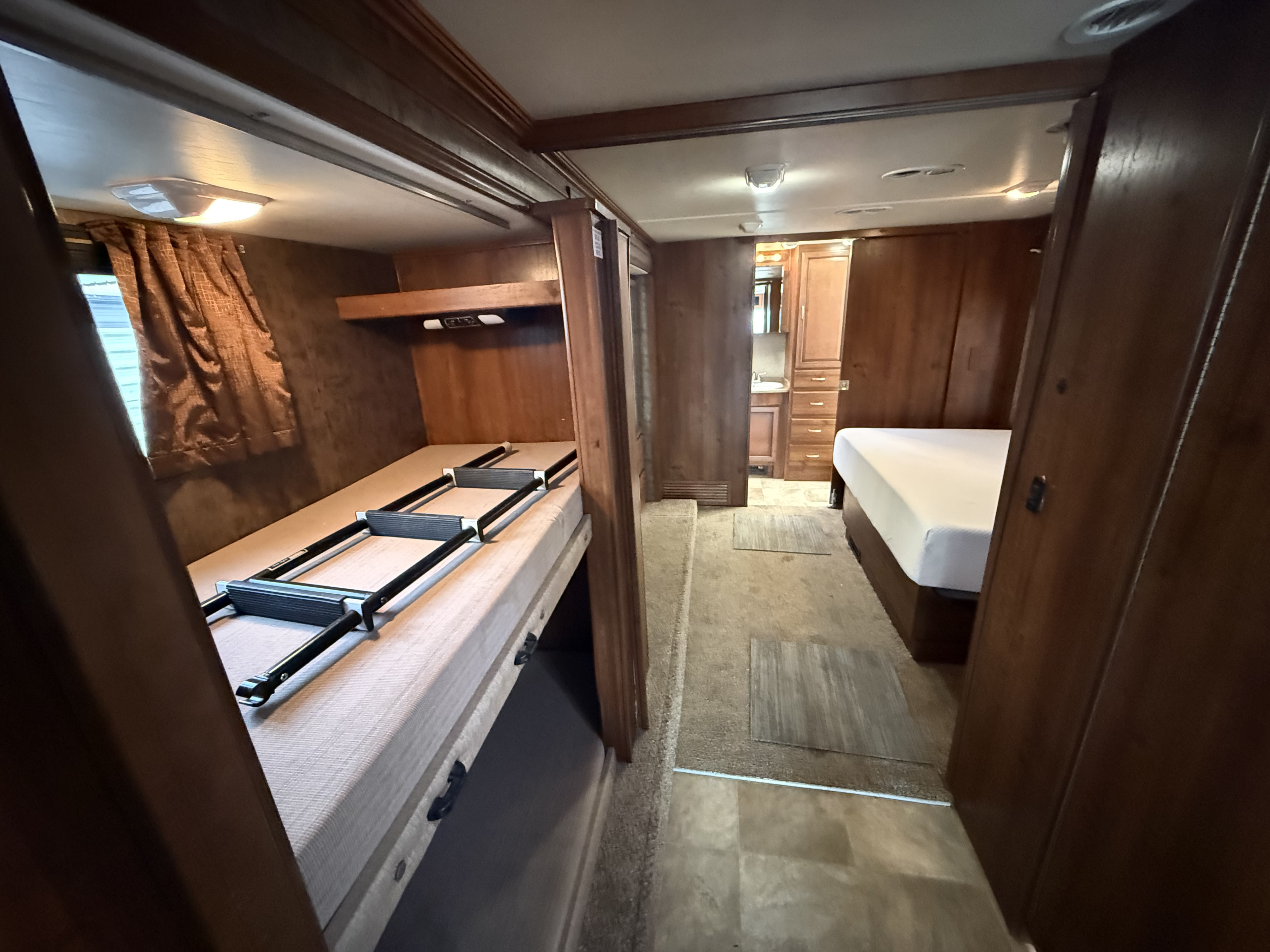 Cozy RV rental interior: bunk beds with ladder, hallway leading to master bedroom & bathroom. Warm wooden decor.. Fleetwood bounder 2014