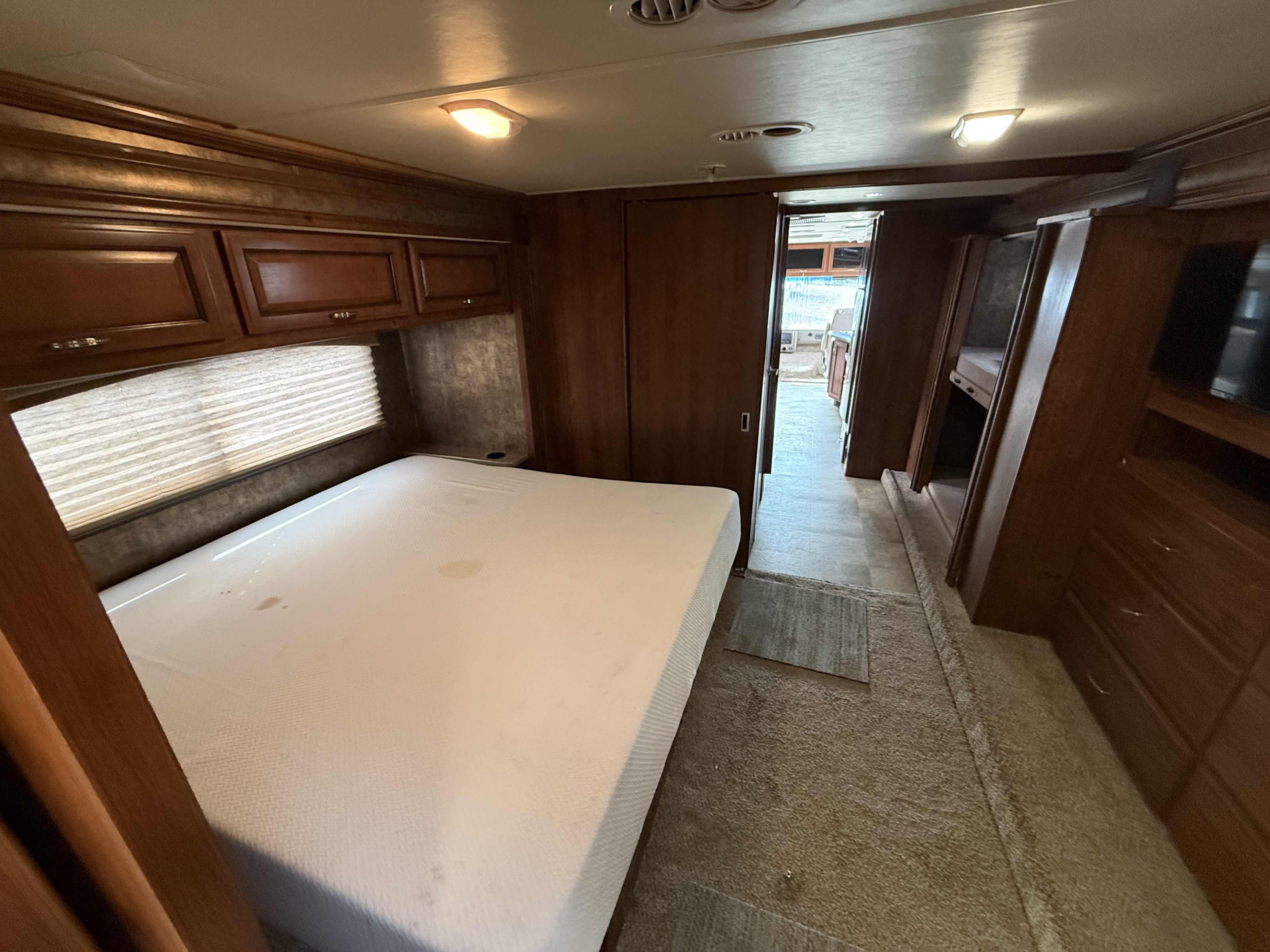 This rv rental features a cozy bedroom with a bed, overhead storage, and hallway access. Notice the mattress stains & ceiling lights.. Fleetwood bounder 2014