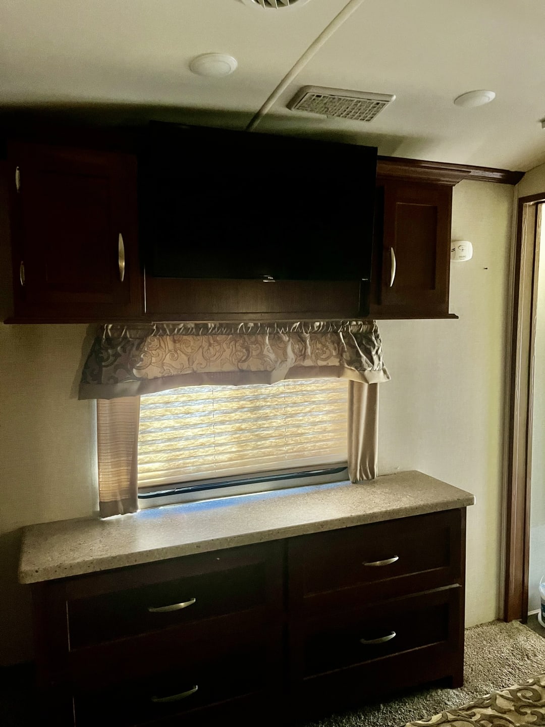 RV rental interior: bedroom with wall-mounted TV, cabinets, & dresser below a window with blinds, creating a cozy travel space.. Forest River Cardinal Blue Ridge Cabin 2017