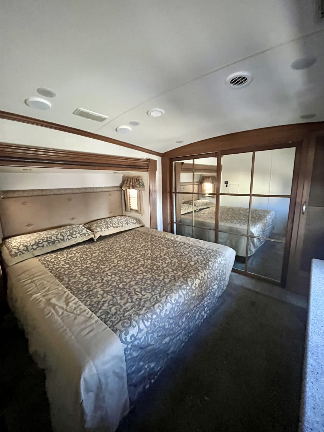 RV rental bedroom with a large, comfortable bed, patterned bedding, padded headboard, and mirrored closet doors.. Forest River Cardinal Blue Ridge Cabin 2017