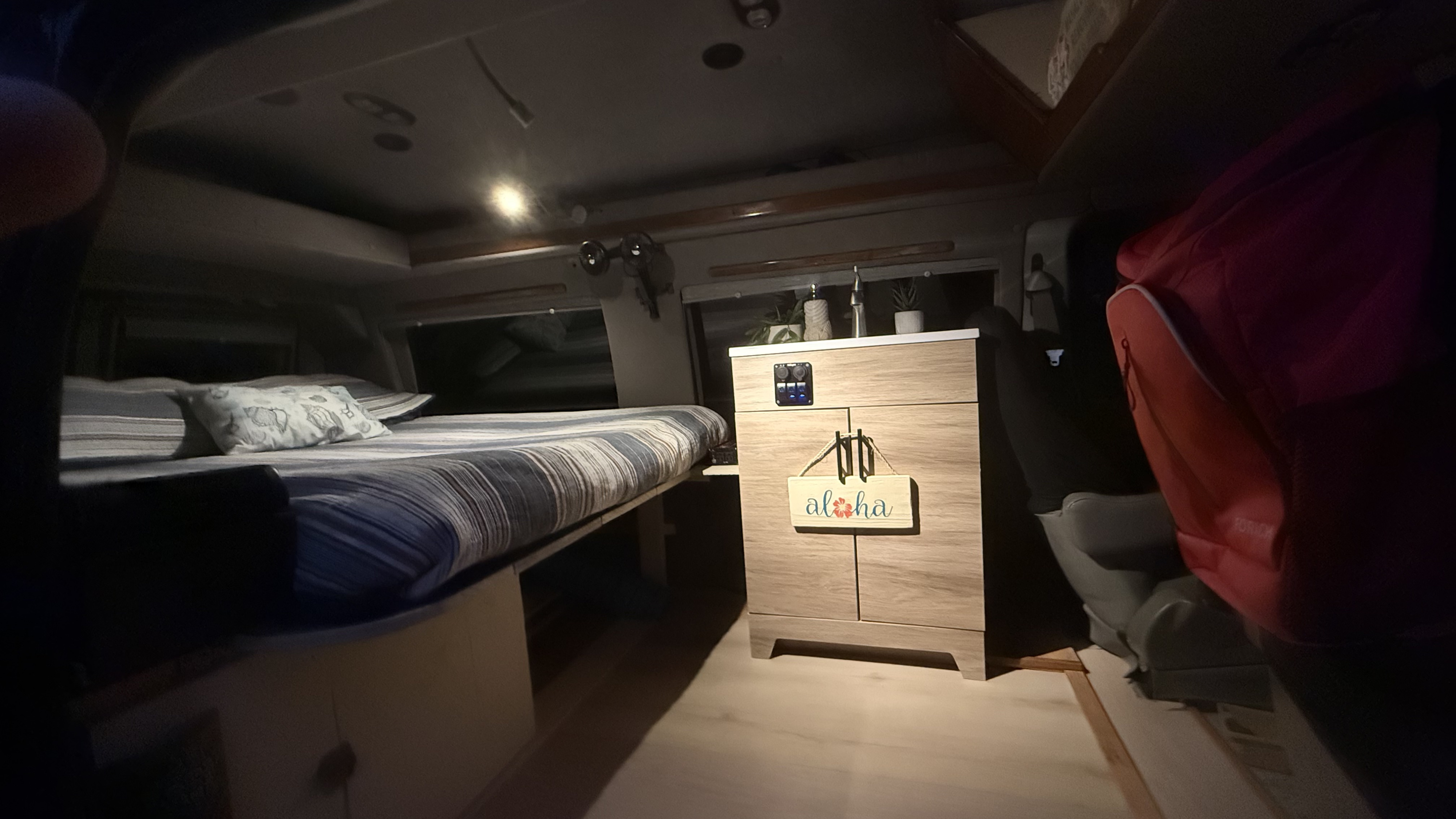 Interior of a cozy RV rental, showing a striped bed, a small kitchen counter with a sink, and an "aloha" sign.. Ford Econoline Club Wagon 2005