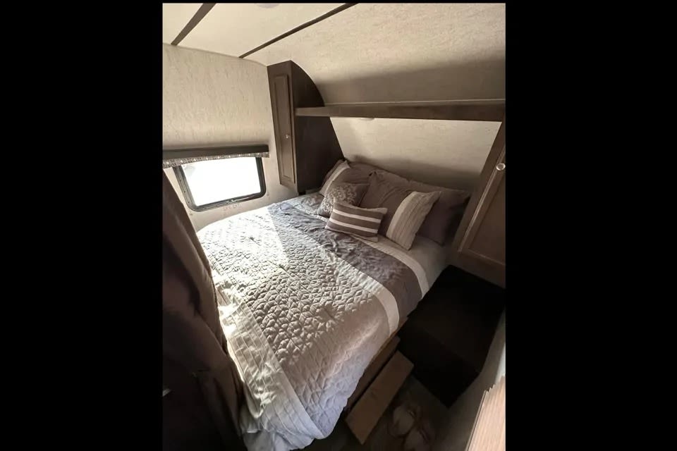 Cozy RV rental bedroom with a neatly made bed, pillows, window, and built-in storage cabinets. Ideal for travel comfort.. Starcraft Autumn Ridge 2018