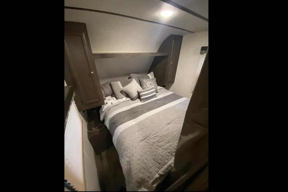 Cozy RV rental bedroom featuring a comfortable bed with gray bedding, pillows, and overhead storage cabinets.. Starcraft Autumn Ridge 2018