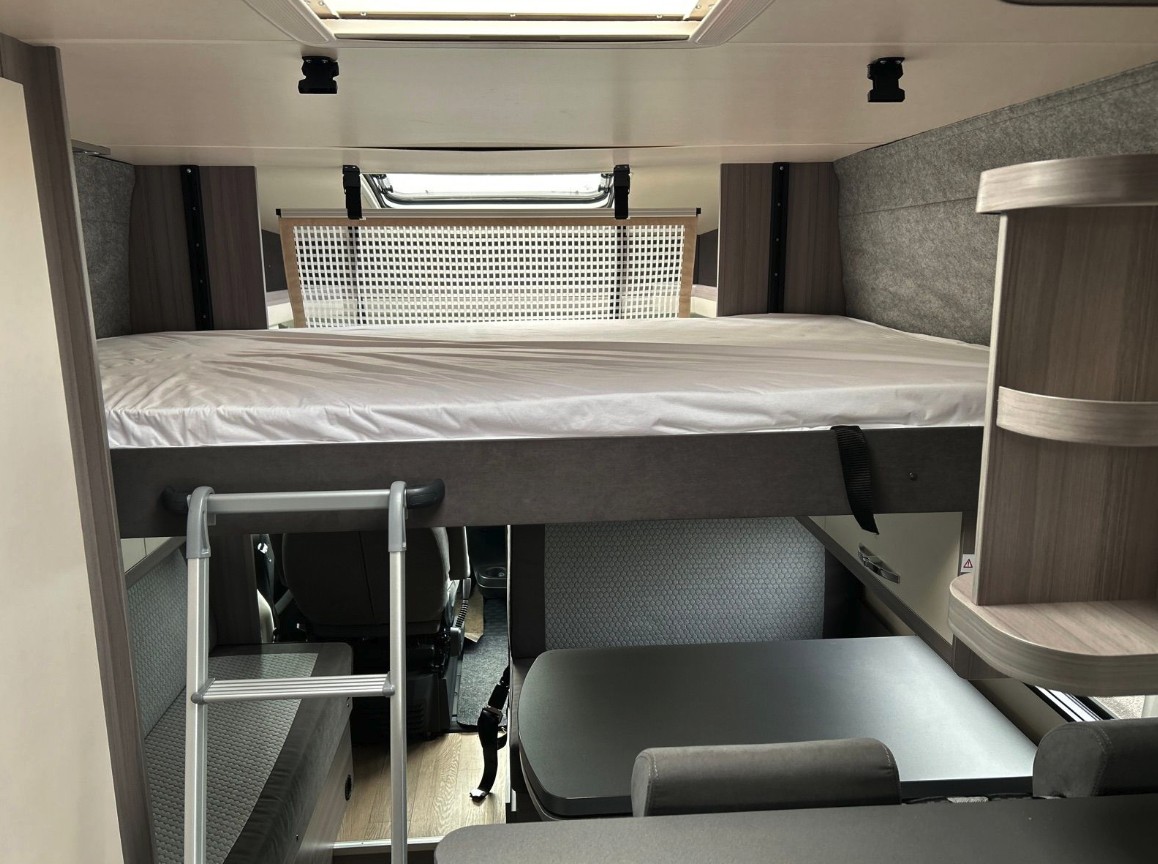 Comfortable RV rental interior with an elevated bed, ladder access, and a cozy dining area below.. Hobby T65 HKM 2024