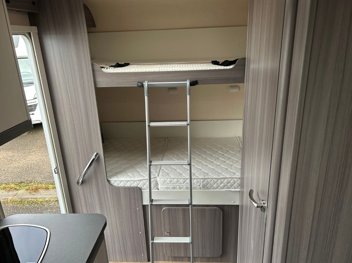 RV rental bunk beds: A compact sleeping area with an upper and lower bed, ladder, and mattresses for family travel.. Hobby T65 HKM 2024
